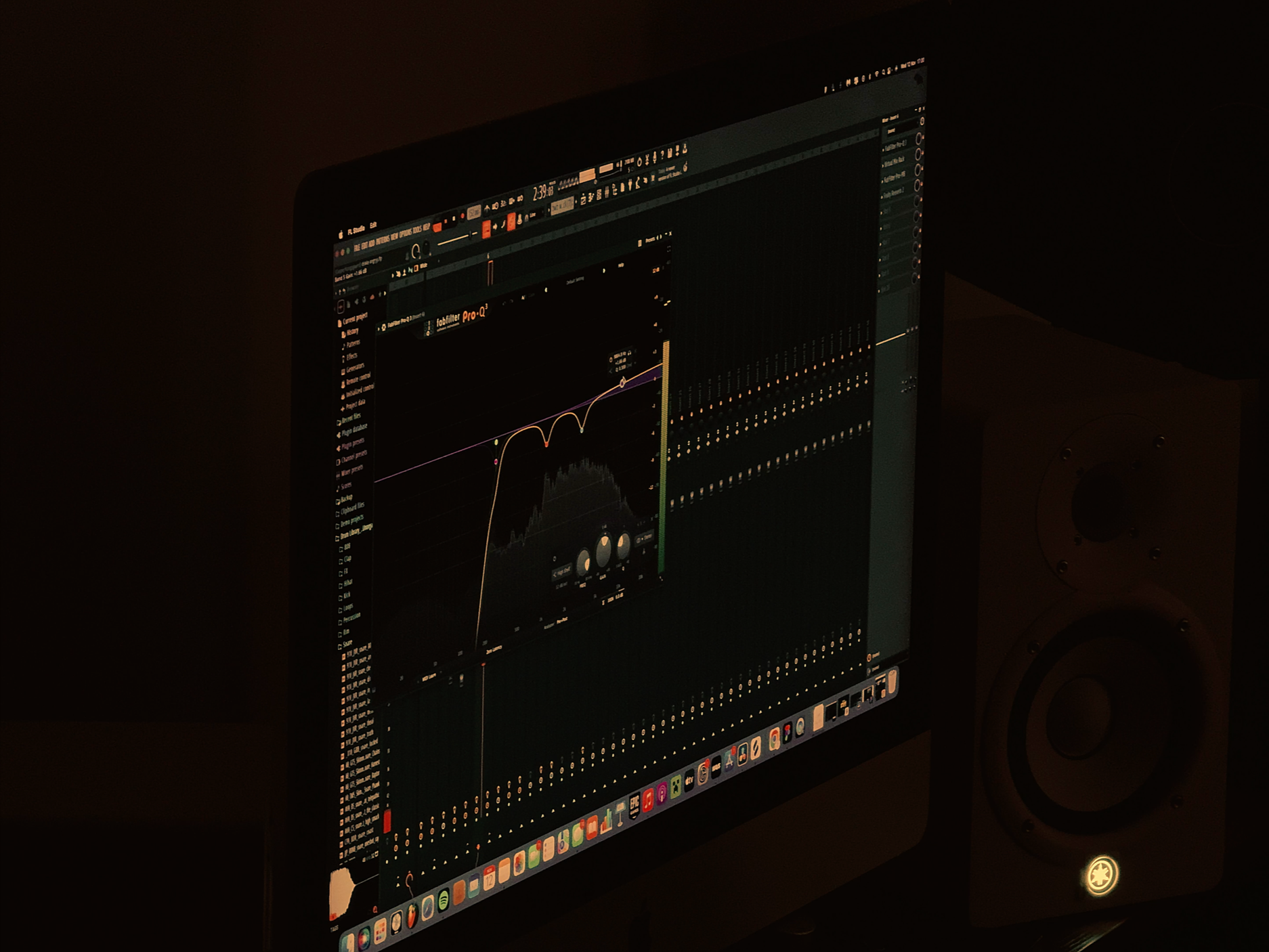 A computer monitor displaying an audio editing software with a digital equalizer and multiple tracks. A speaker is visible to the right of the monitor in a dimly lit room.