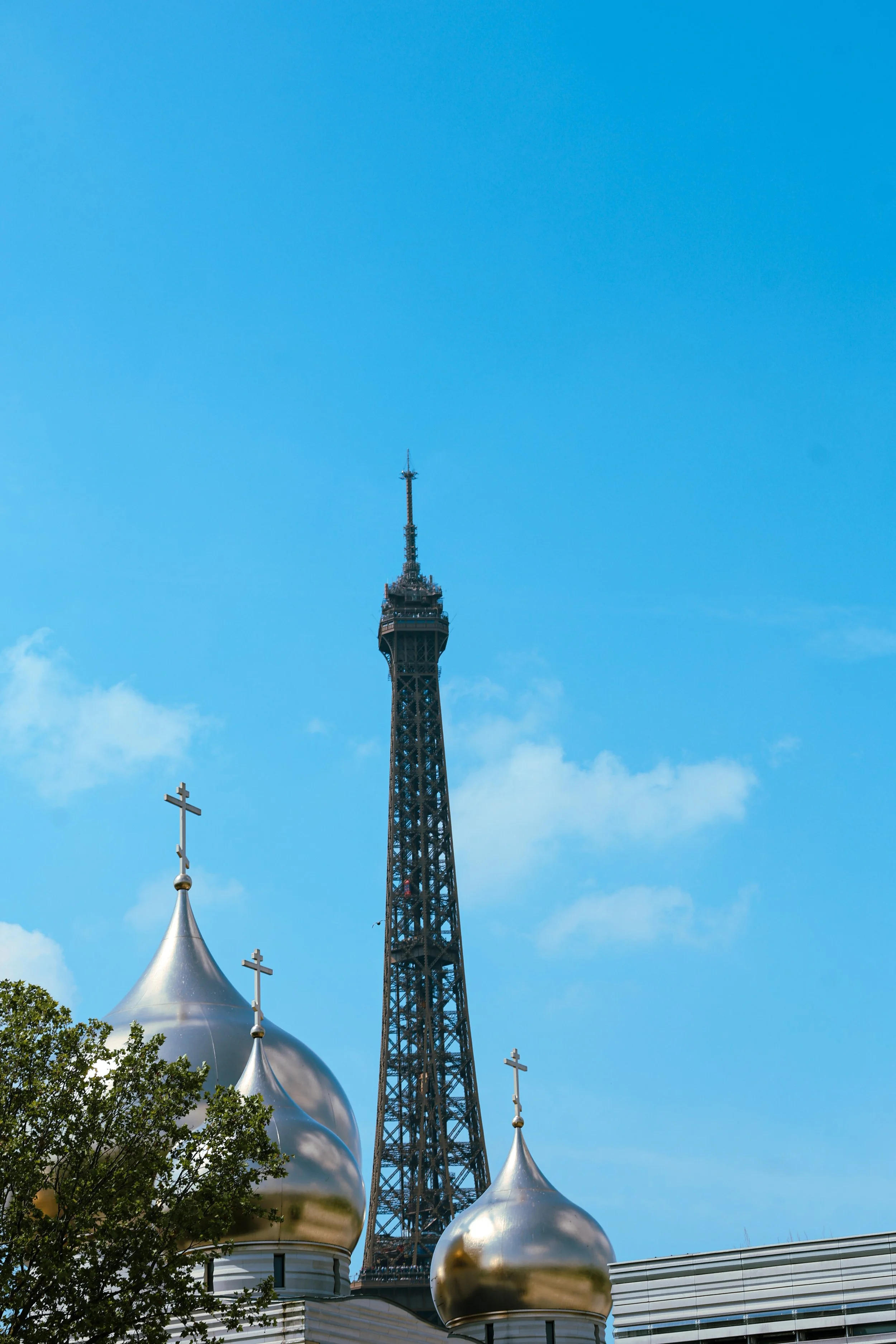 A tall telecommunications tower against a blue sky, with three religious domes topped with crosses in the foreground.
