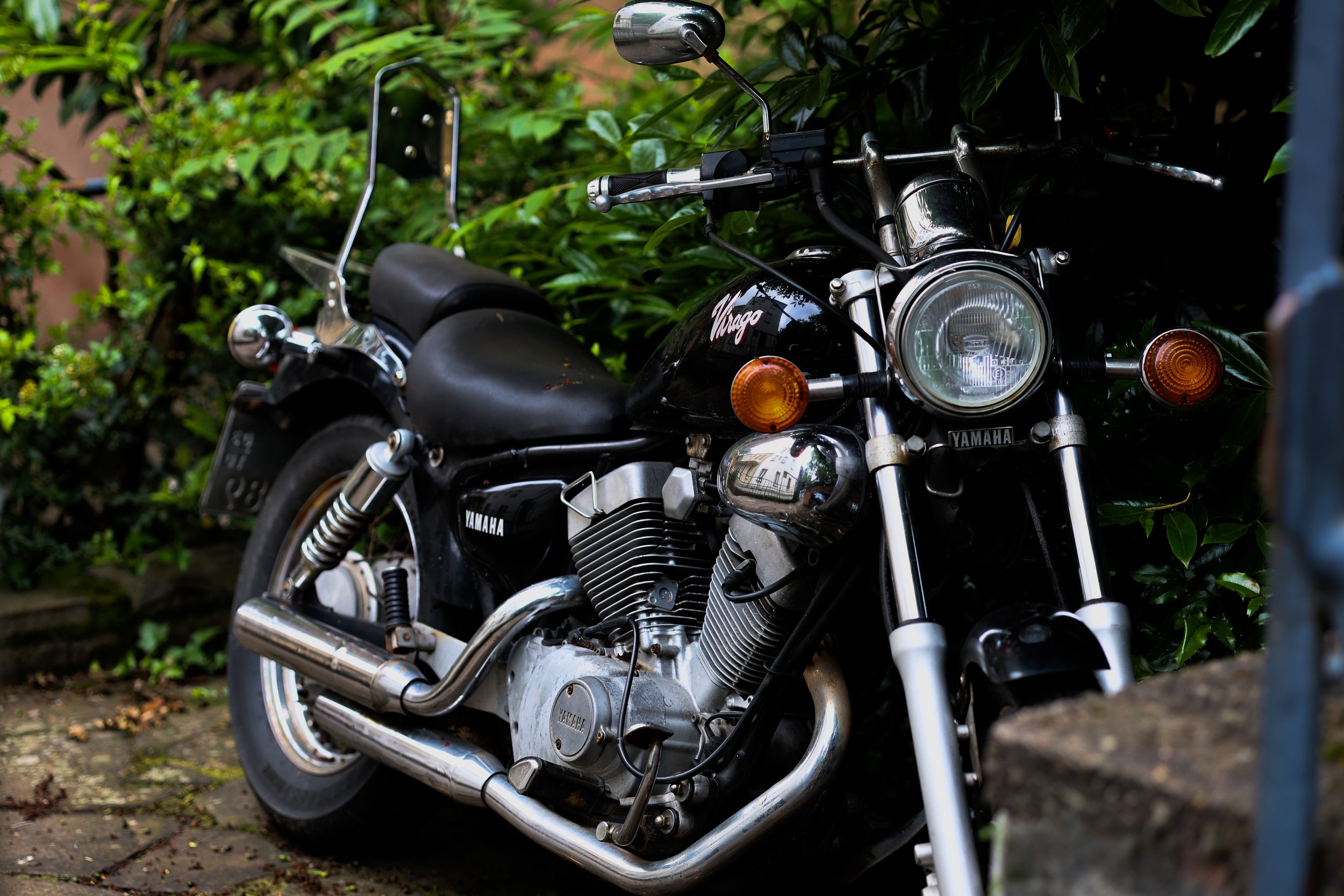 Black Yamaha V Star motorcycle parked on a brick surface with greenery in the background.