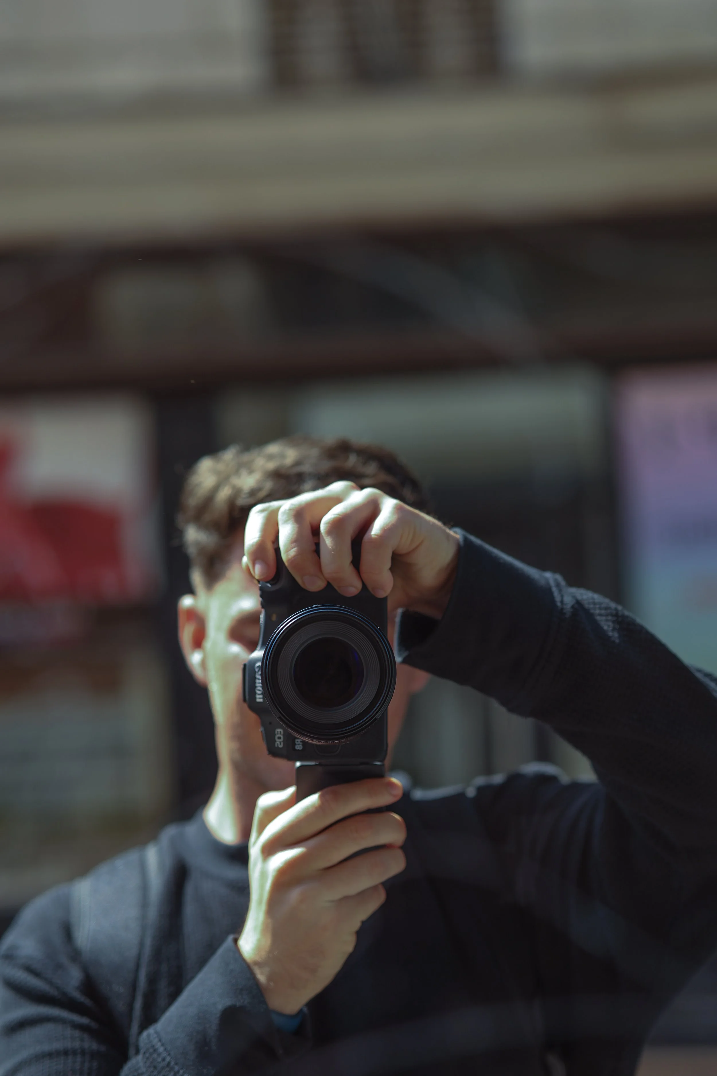 A person taking a photo with a camera, reflected in a mirror, holding the camera with one hand and wearing a black long-sleeve shirt.