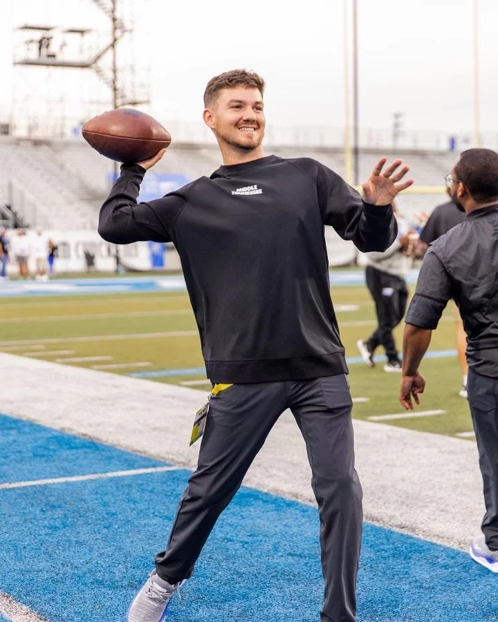 A young man smiling and preparing to throw a football on a sports field.