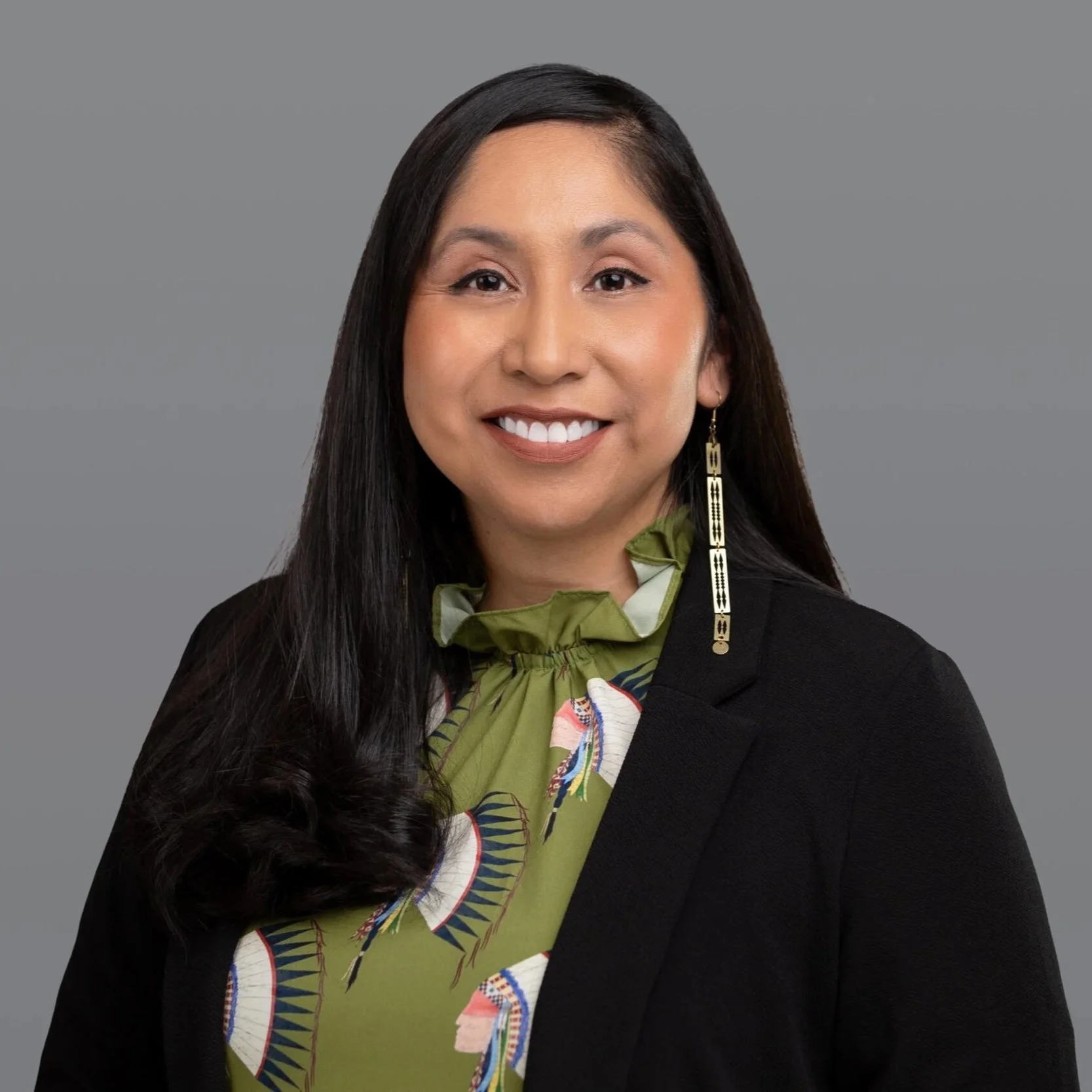 Raelene Whiteshield, Director, smiling in black blazer and green blouse against gray background.