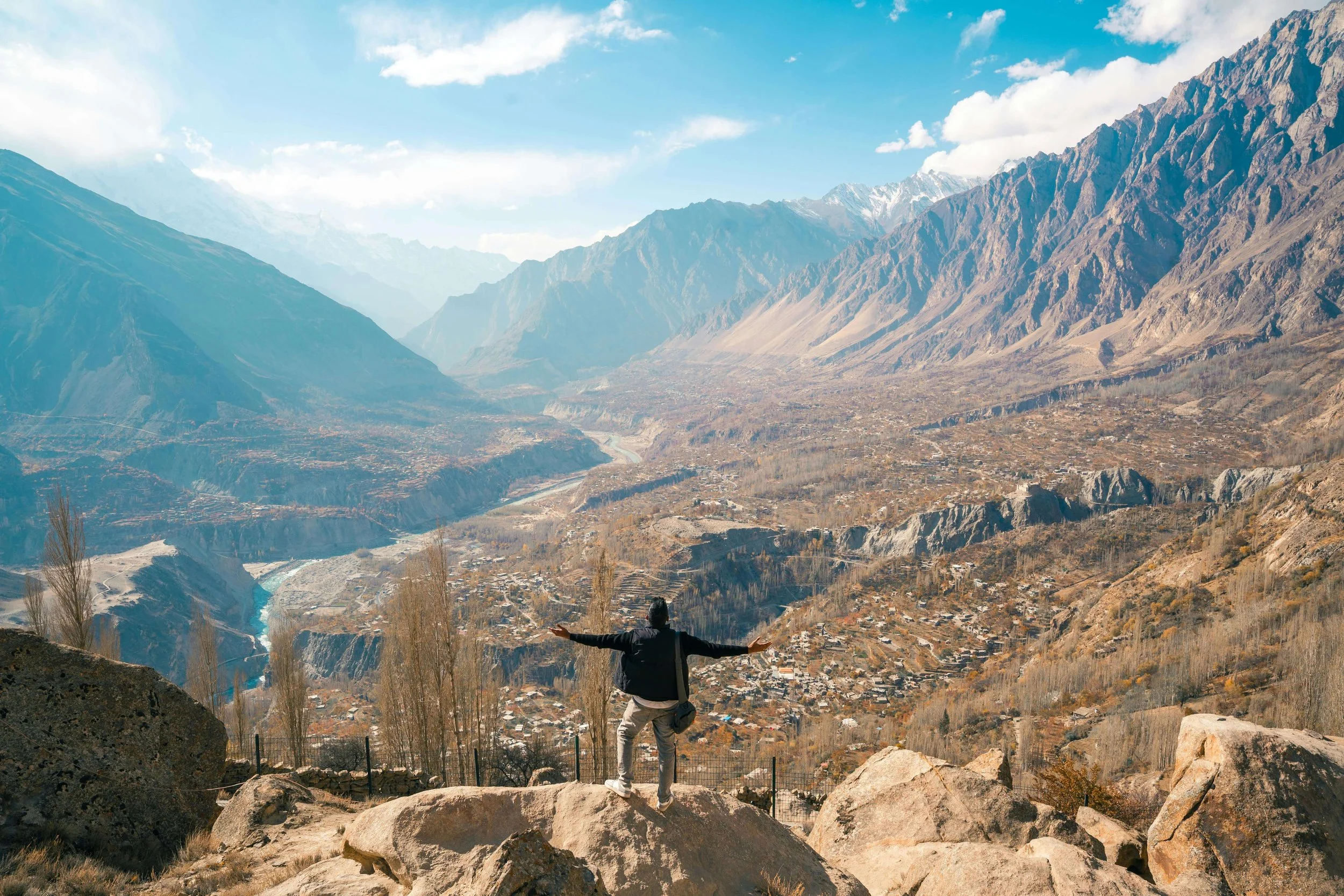Person standing on rocks with arms outstretched overlooking a valley with mountains in the background.