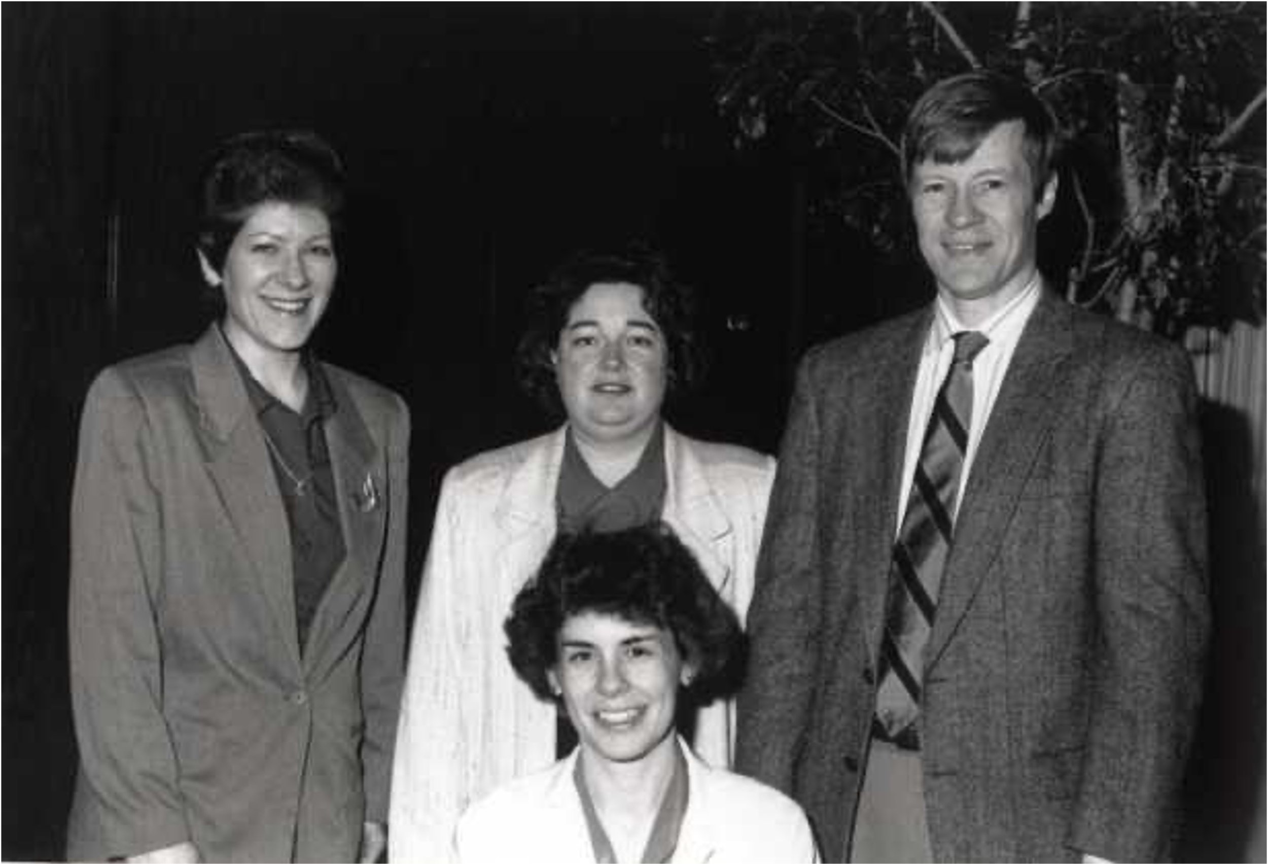 A group of five women and one man dressed in formal attire, posing together outdoors at night, smiling for the camera.