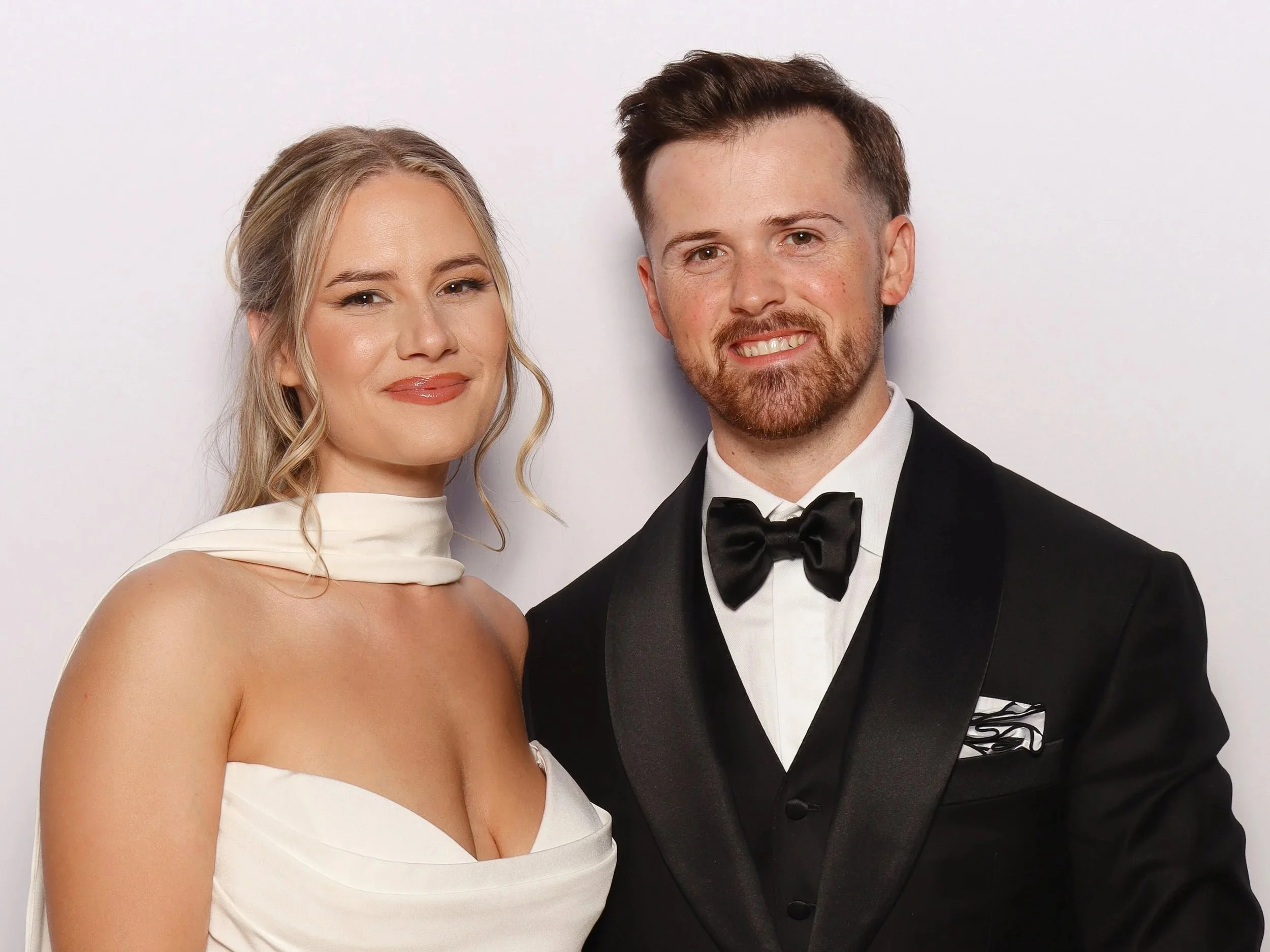 A smiling couple dressed in formal wedding attire, standing against a plain white background for a photo booth in Las Vegas