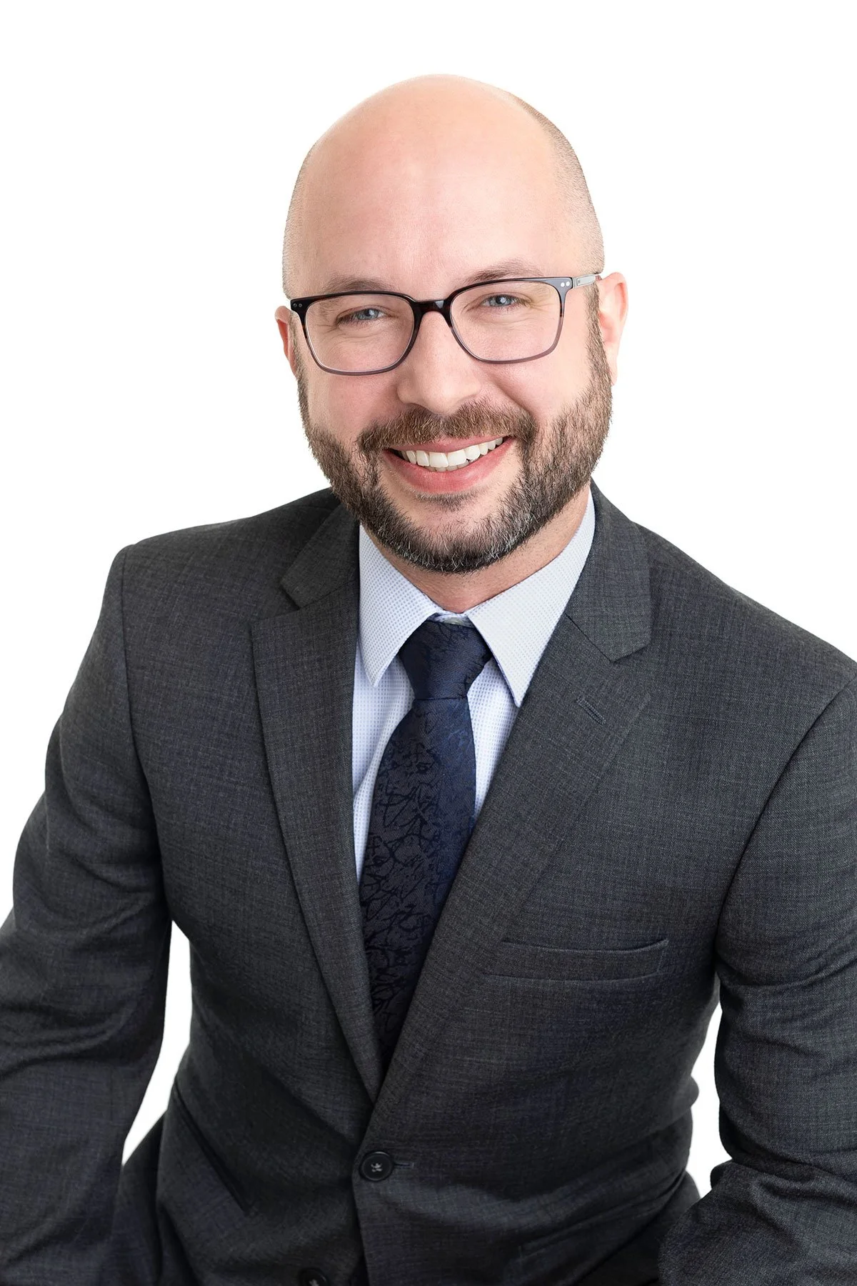 A smiling man with glasses in a suit and tie, posing against a white background.