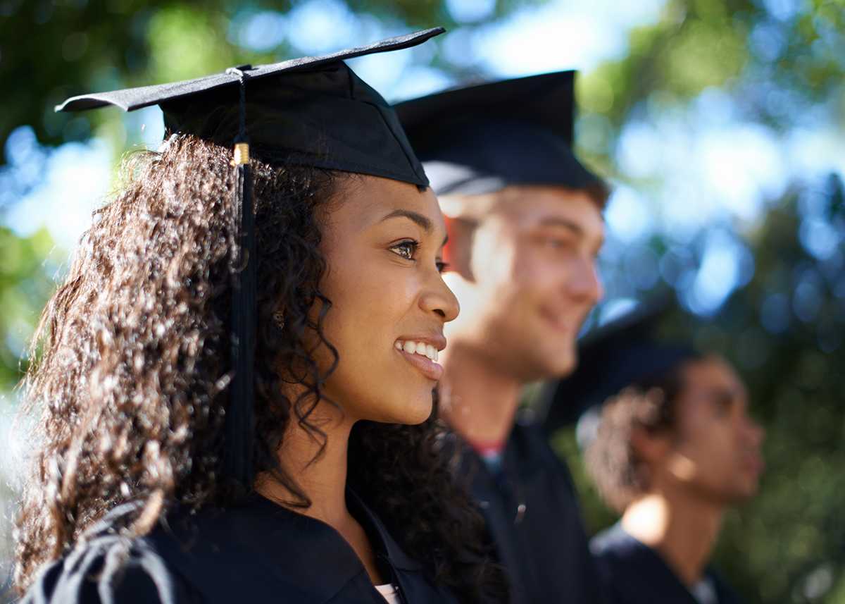 Graduates wearing caps and gowns standing outdoors with trees in the background.