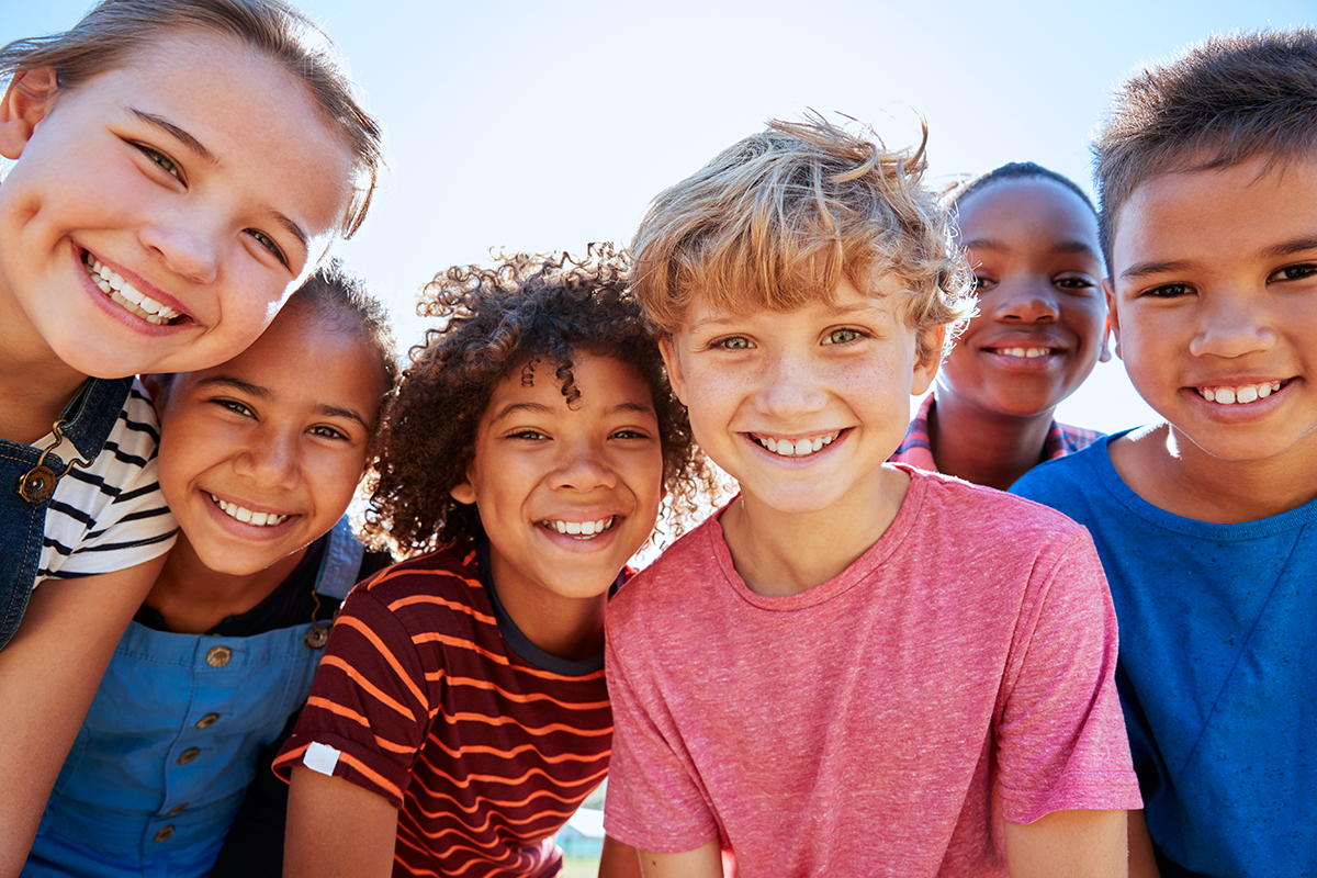 Group of kids smiling and posing together outdoors.