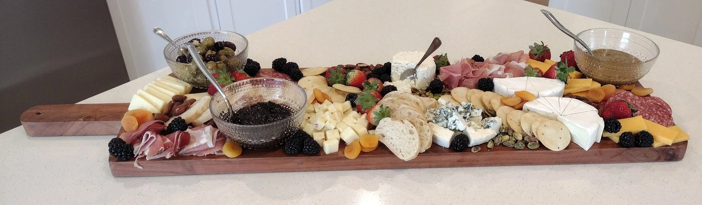 Cheese platter with assorted cheeses, meats, fruits, nuts, bread, and dipping sauces on a wooden board.