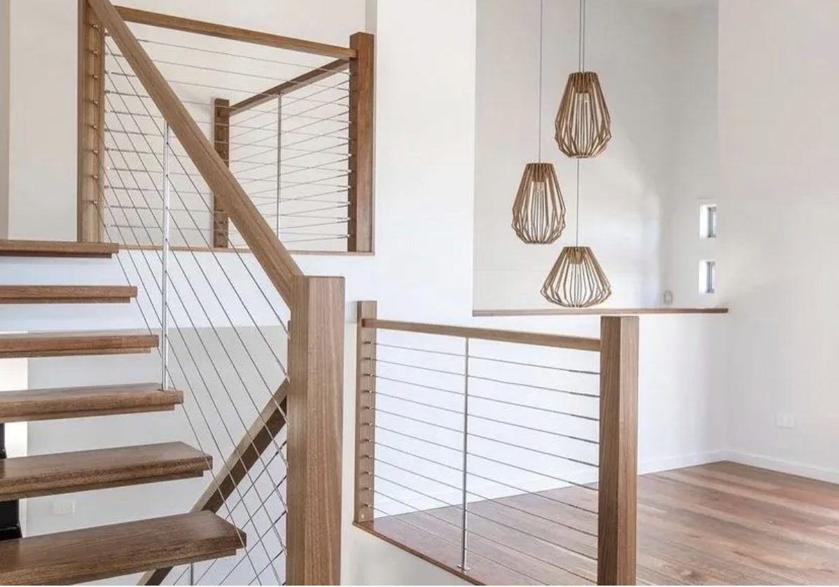 Interior view of a modern staircase with wooden steps, metal railing cables, and wooden handrails, with a decorative wooden pendant light fixture hanging from the ceiling.
