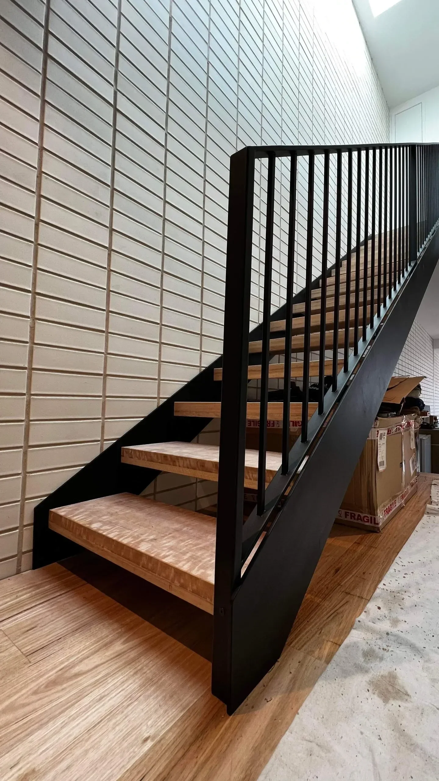 A staircase with wooden steps, black metal frame, and black metal railing beside a white brick wall.