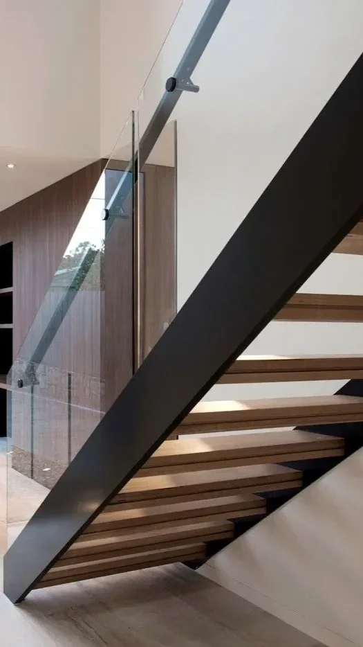 Interior view of a modern staircase with wooden steps and glass railing inside a contemporary home.