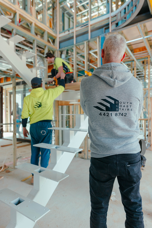 Construction workers installing a staircase inside a building under construction, with a supervisor observing.