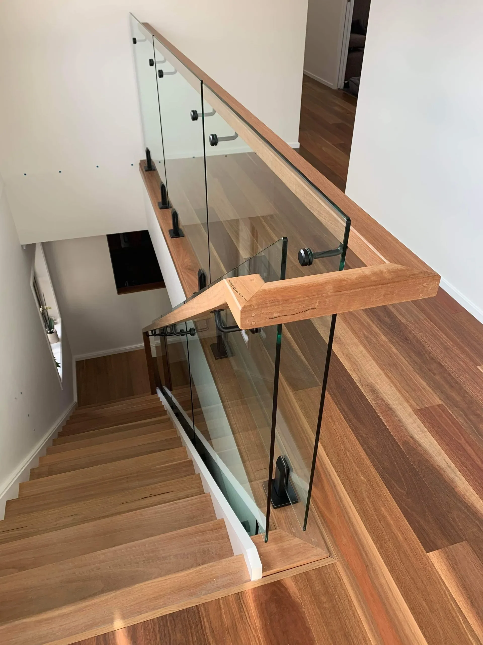 View of a staircase with wooden steps and a glass railing with wooden handrails in a modern house.