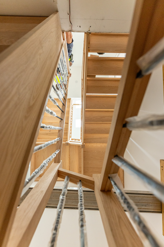 View looking down a wooden staircase with metal railing, showing multiple floors and a child climbing at the top.