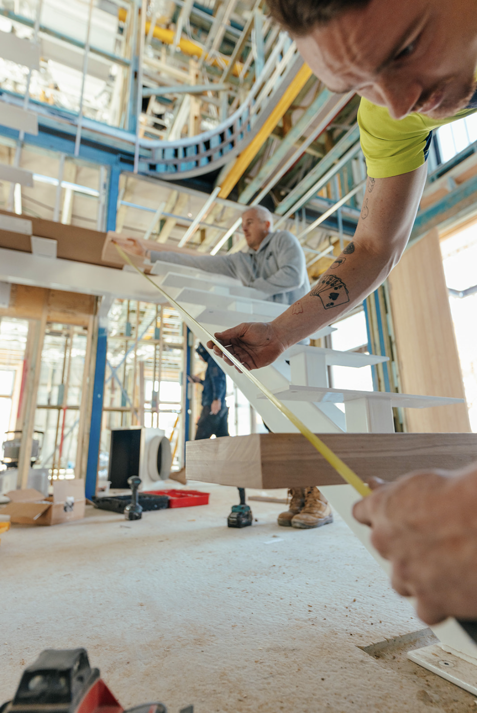 Construction workers measuring and installing staircase in a building under construction with exposed framing and curved ceiling.