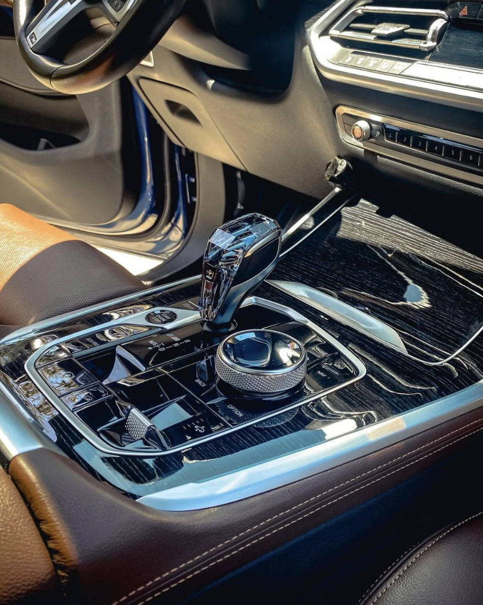 Inside a luxury car, showing the gear shift, control dials, and dashboard with a sleek, modern design and black interior.