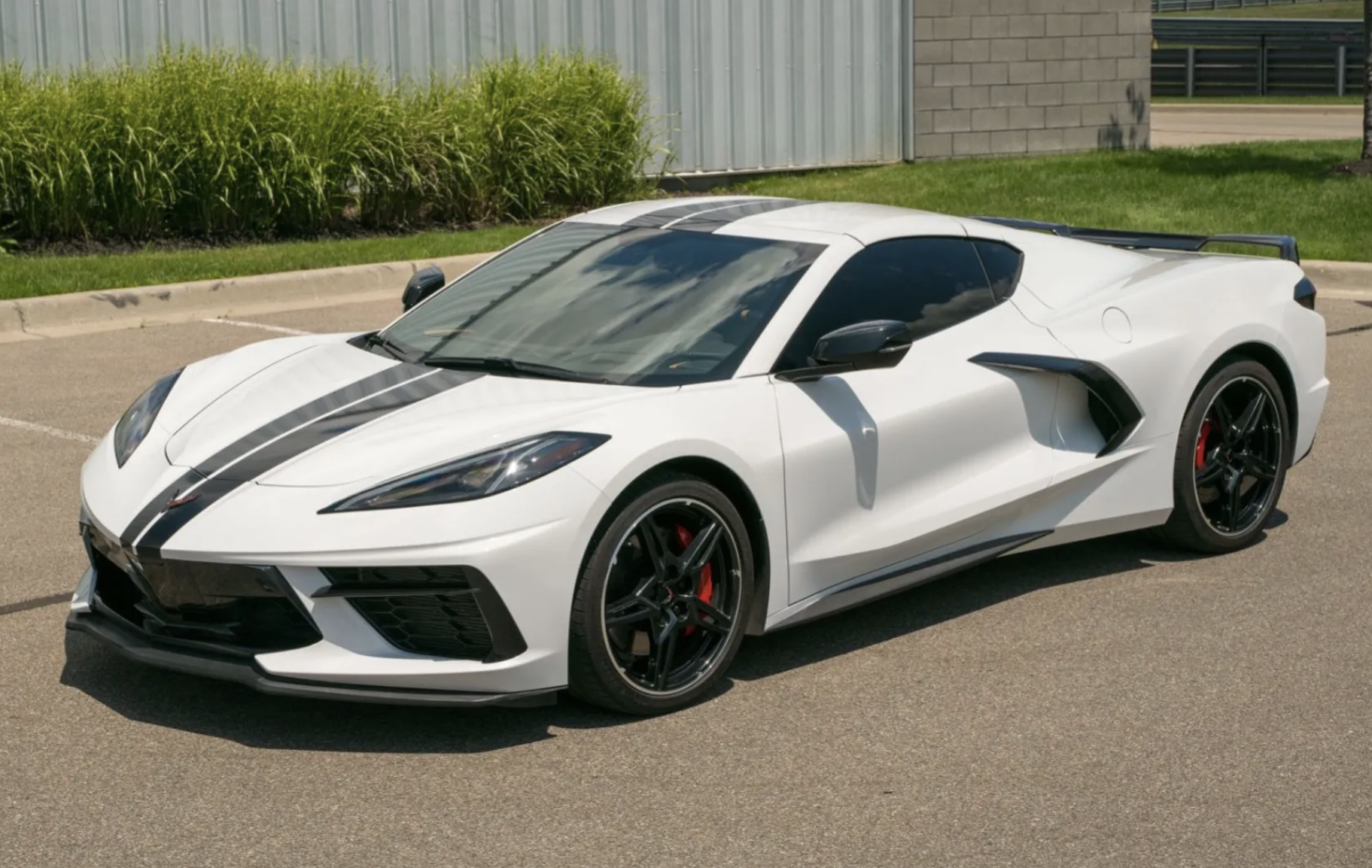 White sports car with black racing stripe, parked in a lot.