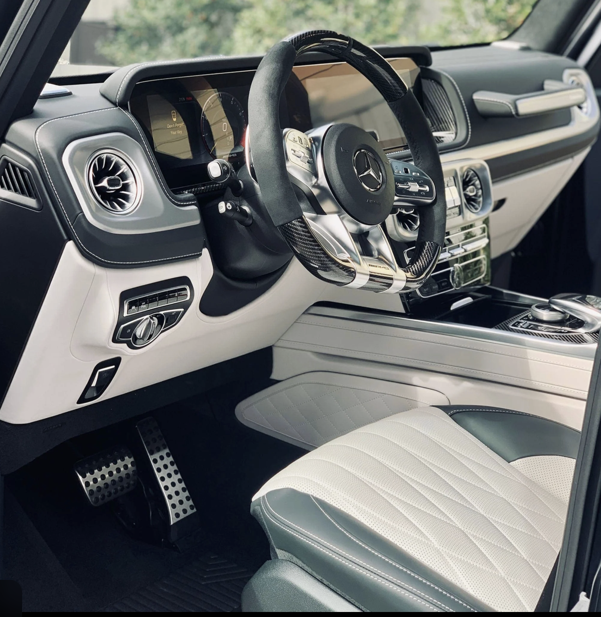 Interior of a luxury Mercedes-Benz vehicle, featuring a modern dashboard with digital displays, a multifunction steering wheel with carbon fiber accents, and a white leather seat with a diamond quilted pattern.