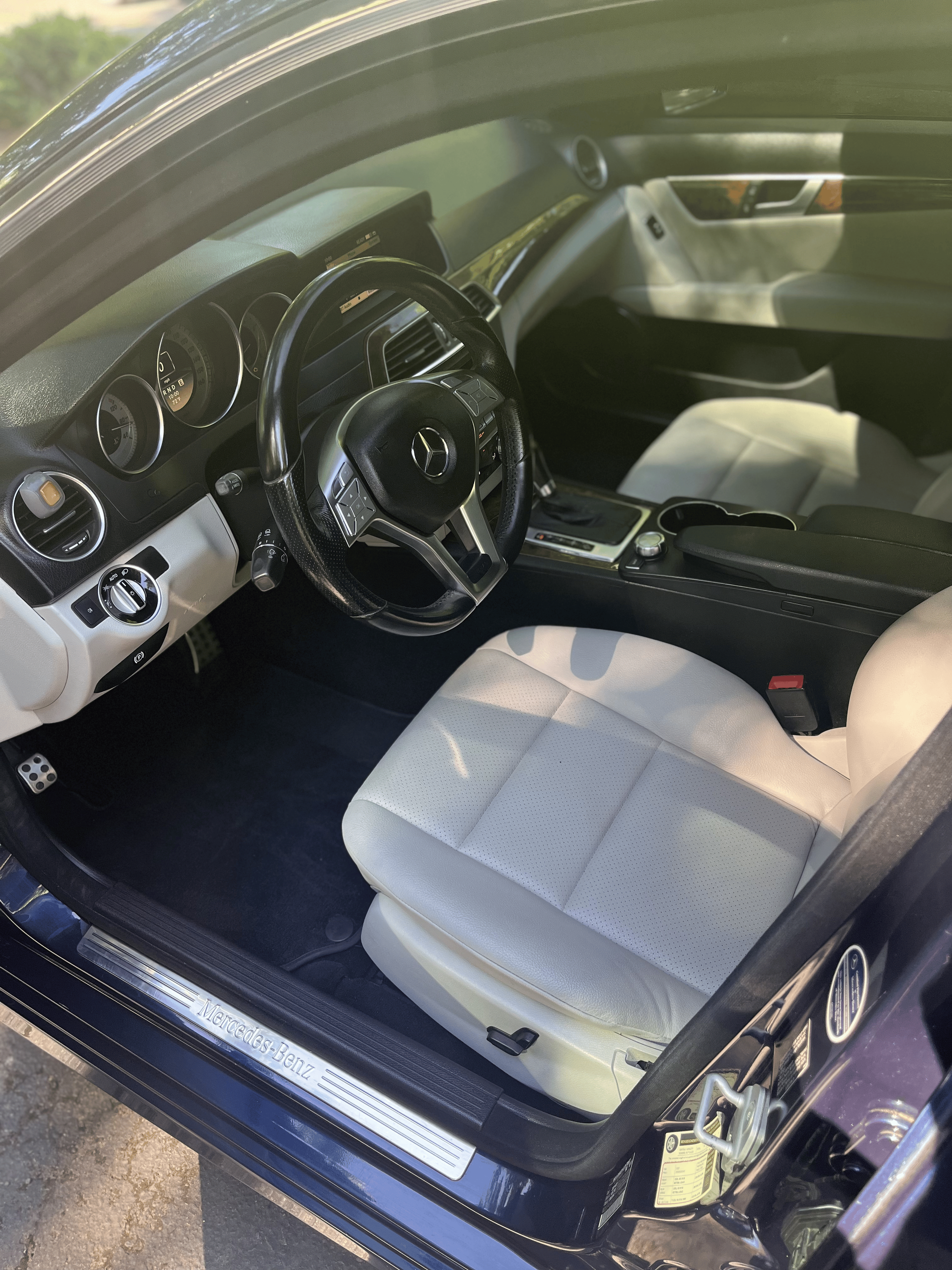 Interior of a Mercedes-Benz car showing a black steering wheel, white leather seat, dashboard, and center console.