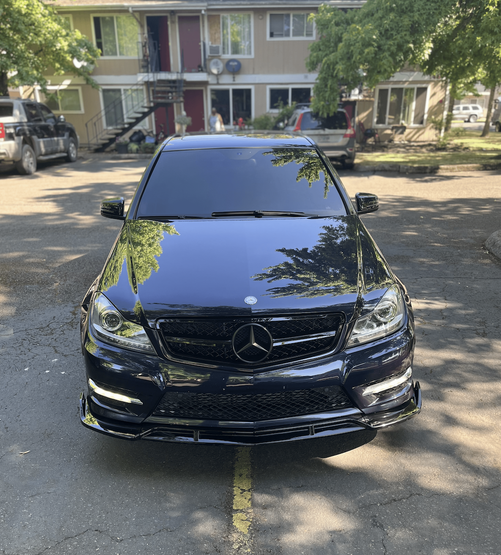 Black Mercedes-Benz car parked in front of a residential building with trees and other parked vehicles visible.