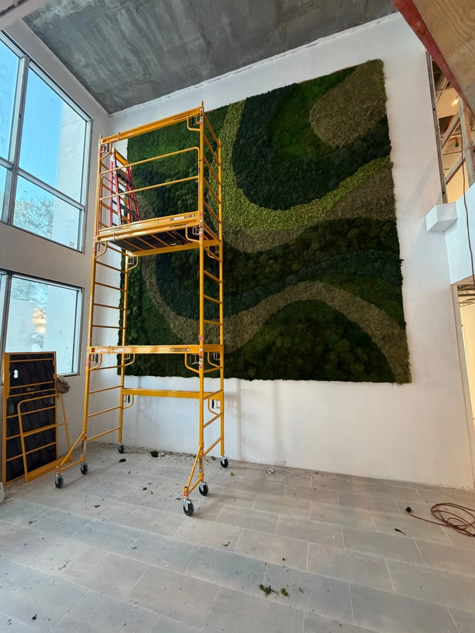 Indoor space with a large textured moss wall art, construction scaffold, and window