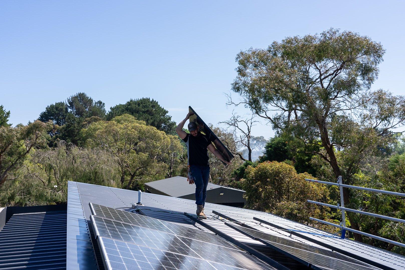 A man installing solar panels on a metal roof surrounded by trees