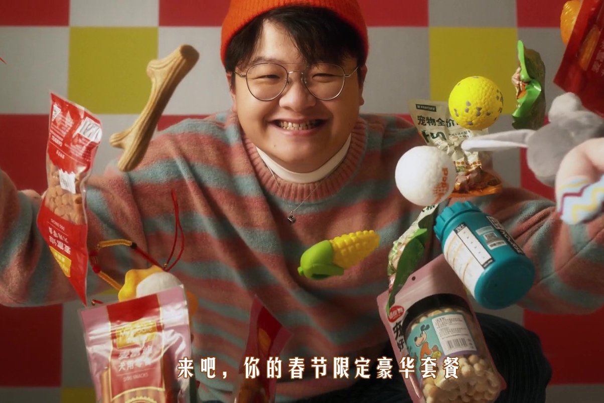 A person smiling and holding a variety of snacks and candies, with a colorful checkered background.