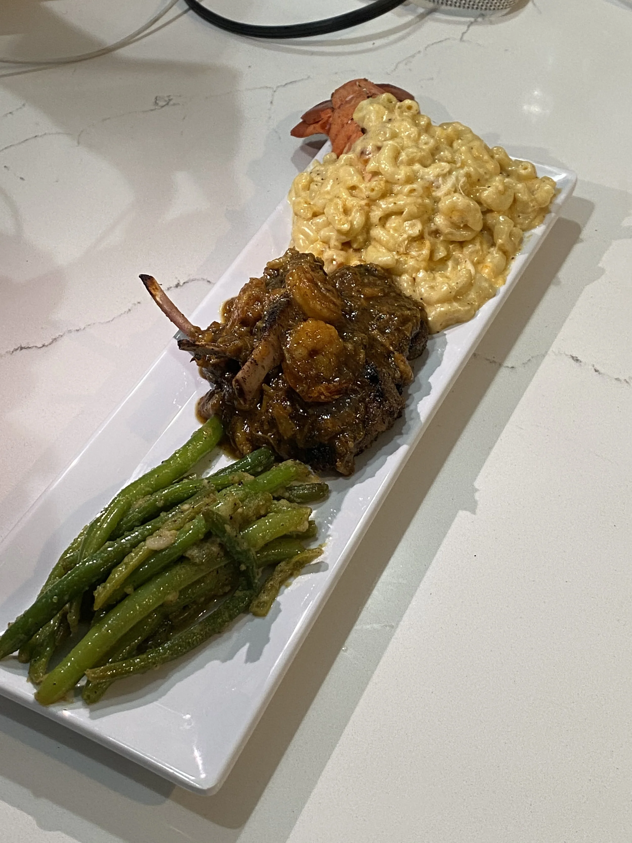 A rectangular white platter containing green beans on the left, a cooked meat dish in the middle, and macaroni and cheese at the top.