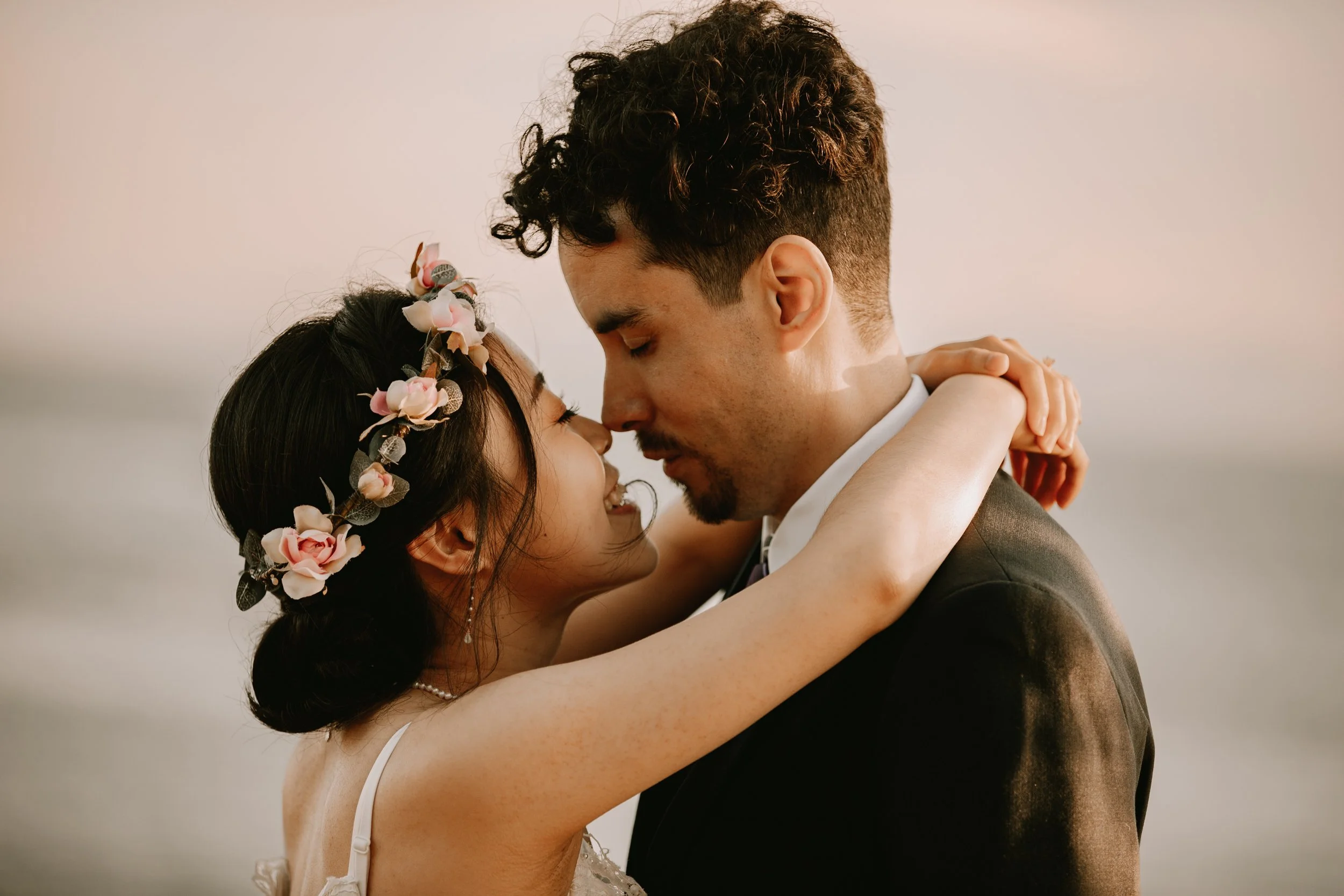A couple embracing intimately, with foreheads touching, during a wedding or romantic moment; the woman wears a floral headband, and the man is dressed in a suit.