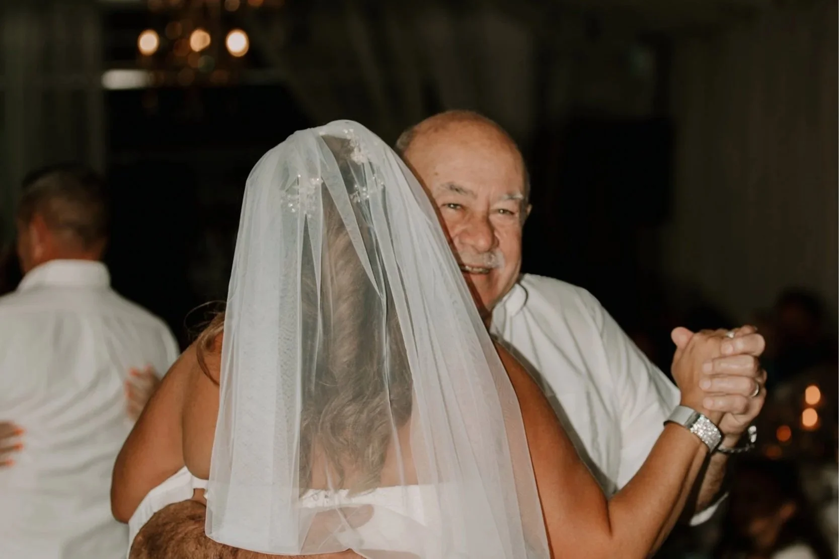 A man and a woman dancing closely at a wedding reception, with the woman wearing a wedding veil and the man smiling.