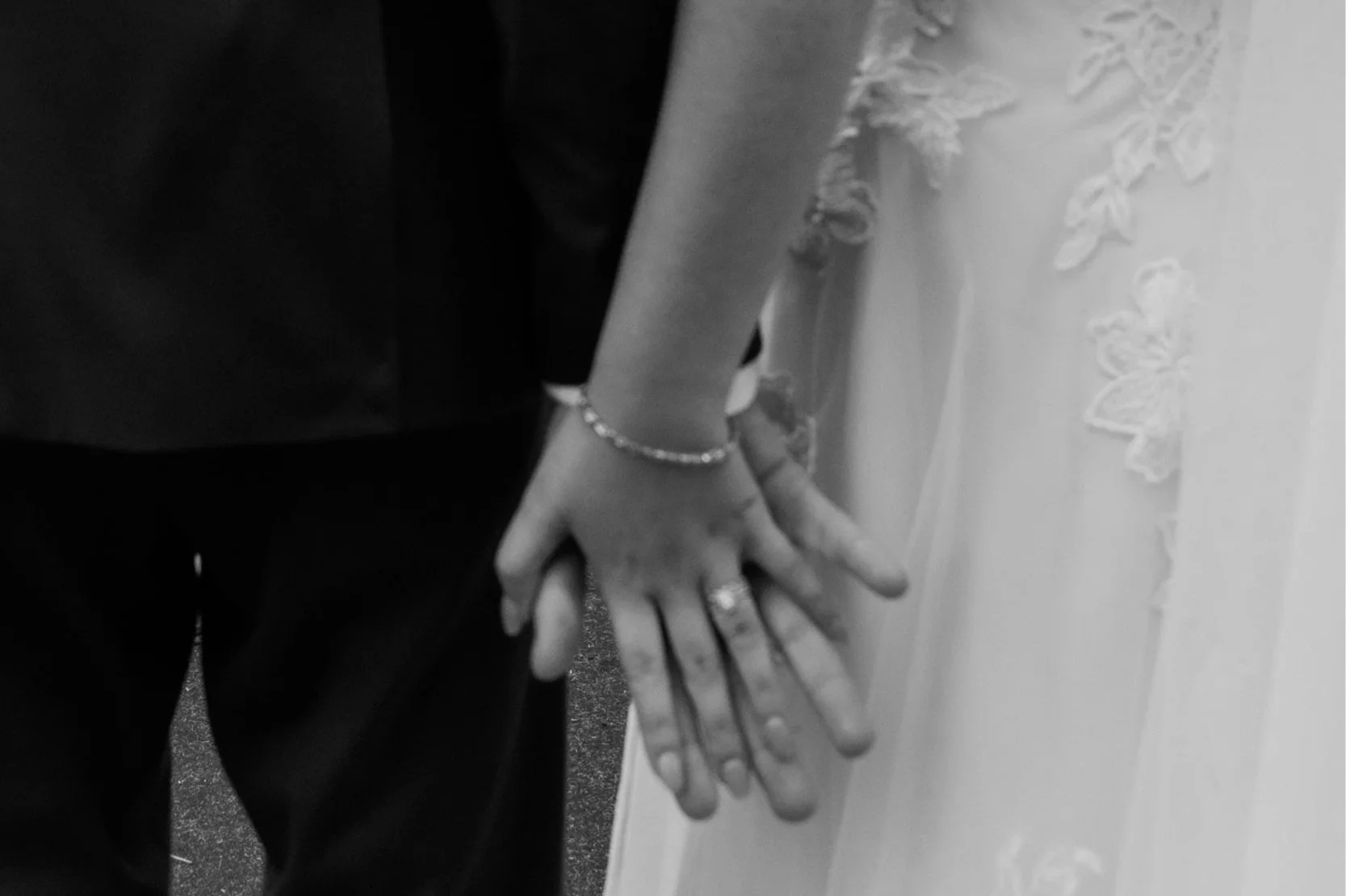 Close-up of a bride and groom holding hands during a wedding ceremony, with the bride wearing a wedding dress with lace details and jewelry.