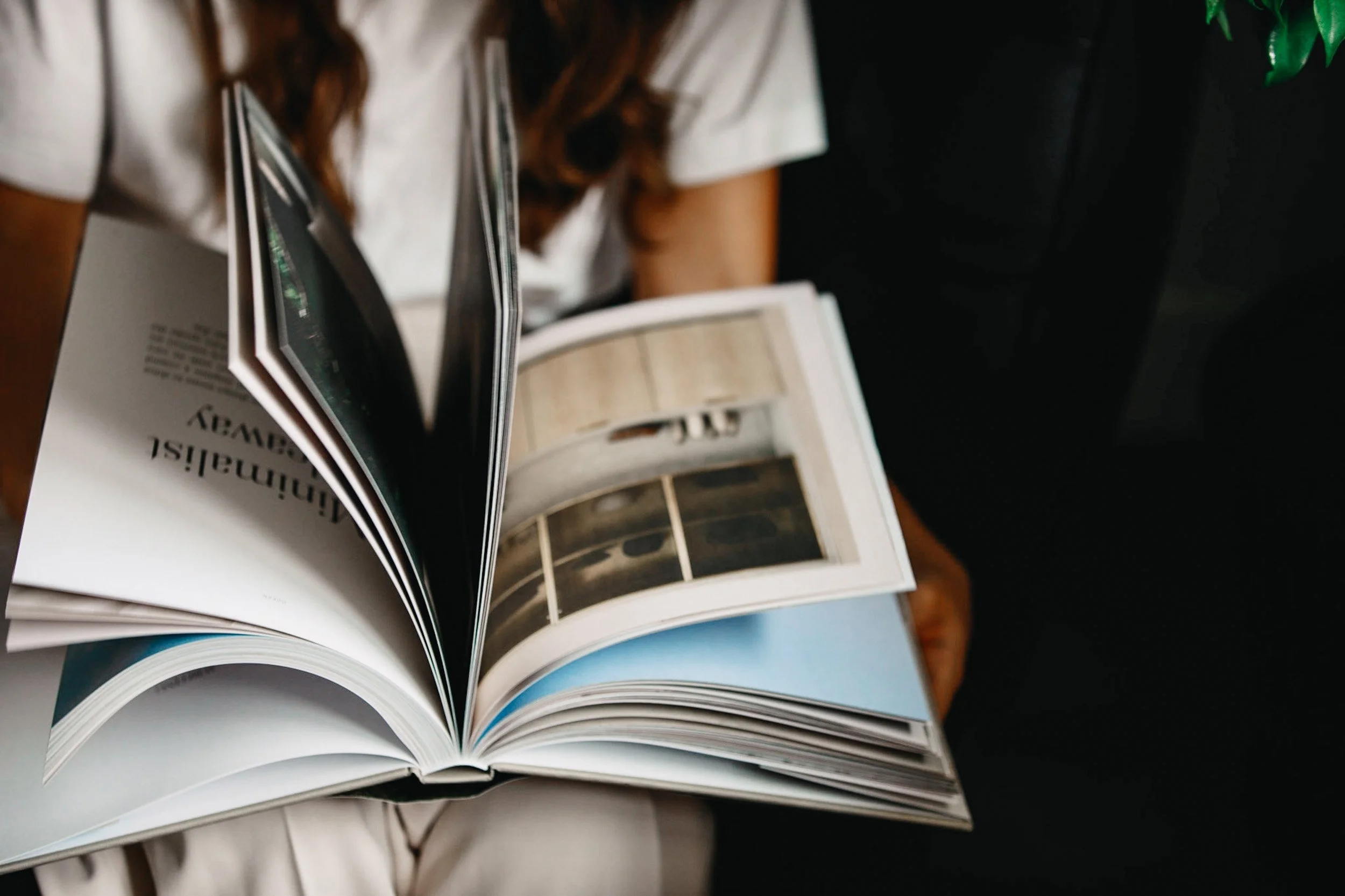 A person flipping through pages in a glossy magazine, showing images of architecture and design.