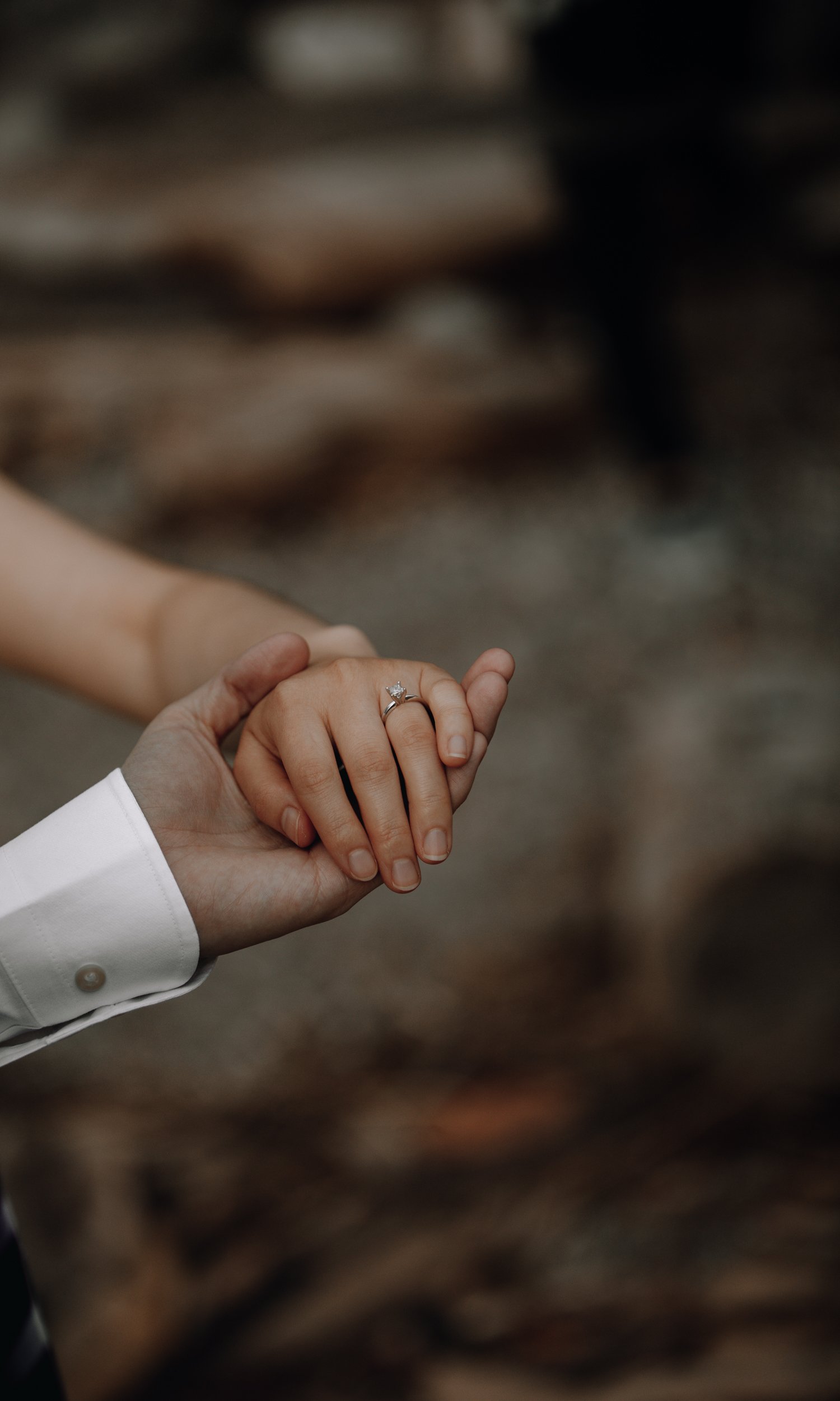 A close-up of a man and woman holding hands, displaying an engagement ring on the woman's finger.