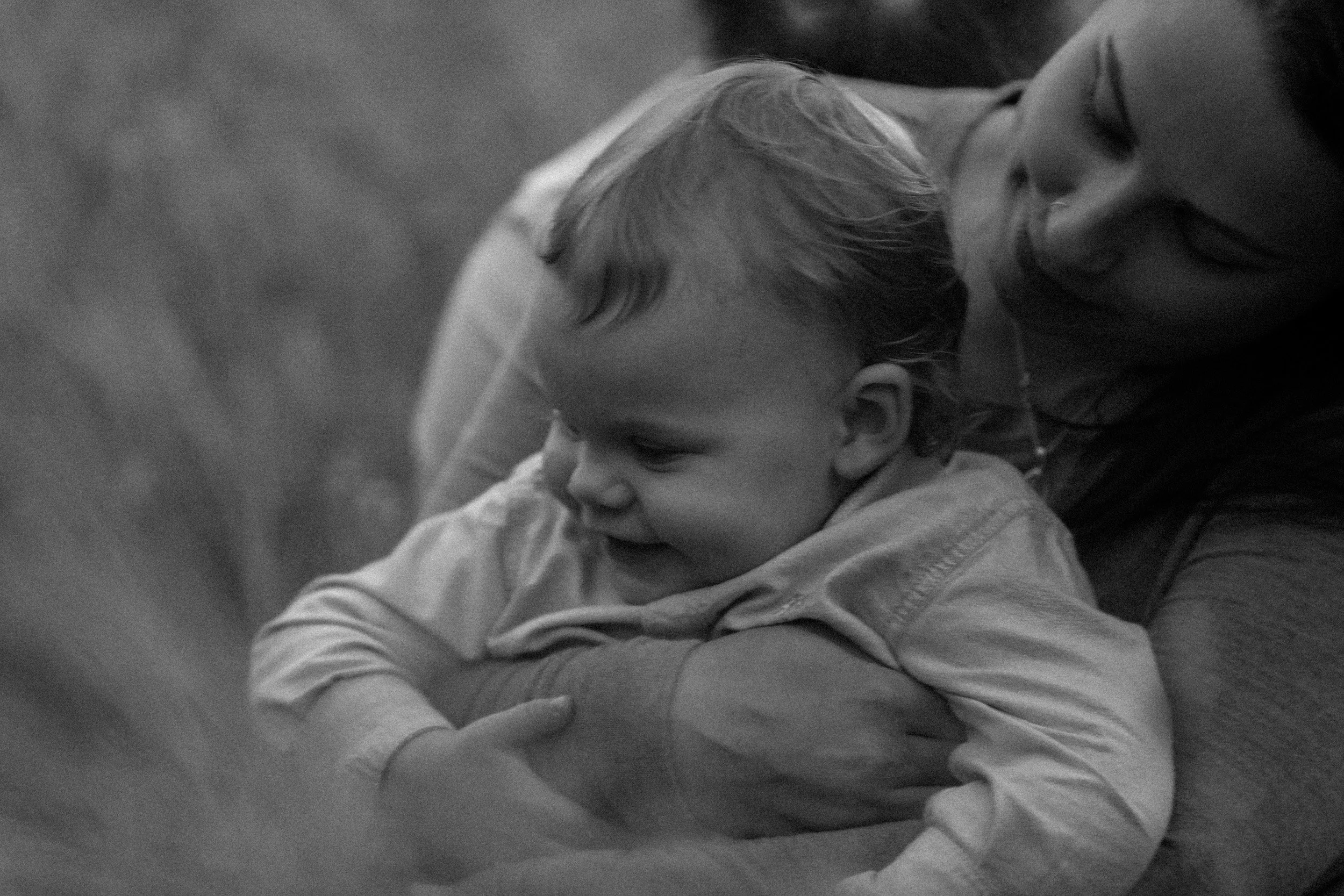 A woman holding a young child, both smiling and engaging with each other outdoors.