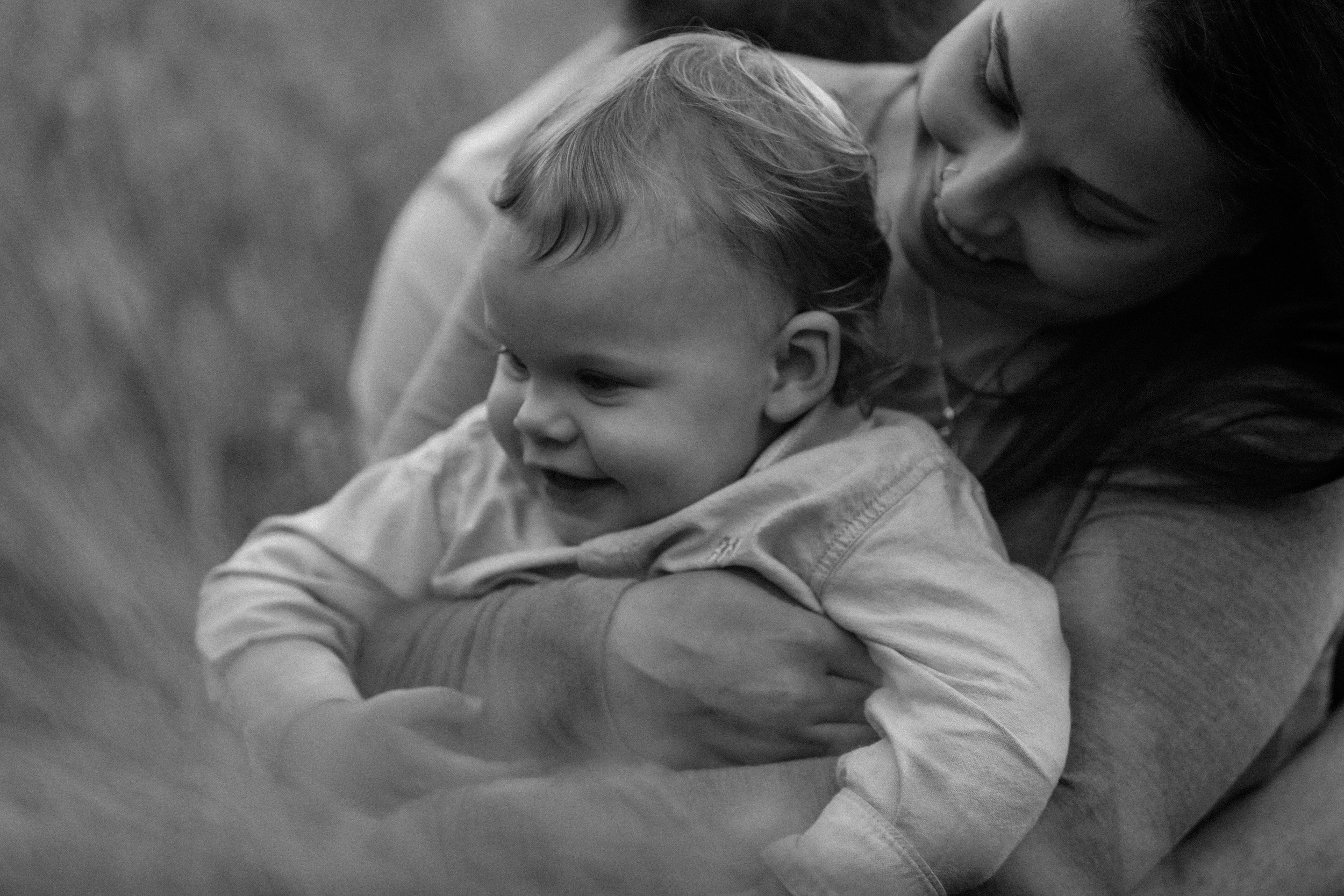 A woman and a young child playing and smiling outdoors.