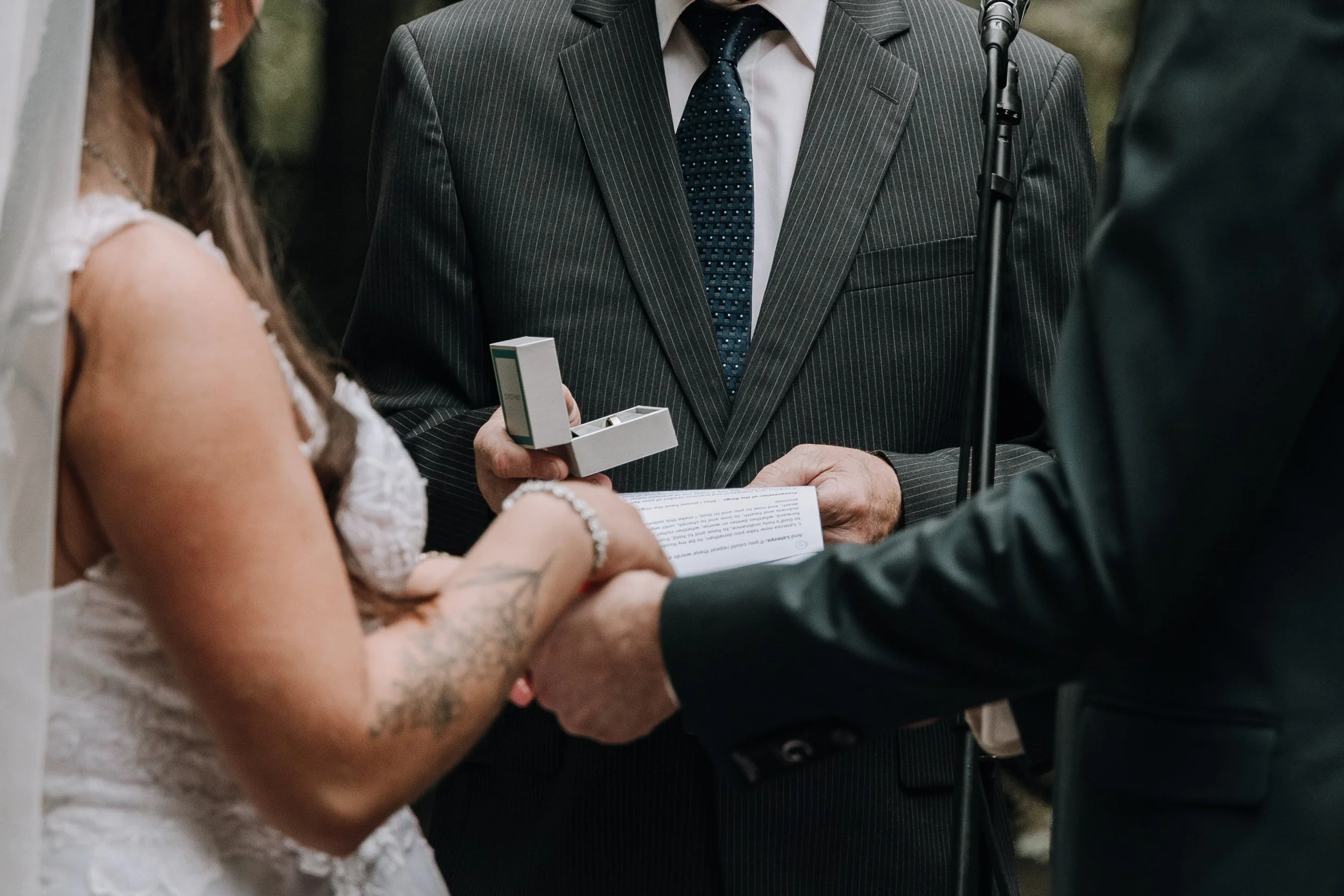 A couple exchanging wedding vows, holding hands, with an officiant reading from a paper, during a wedding ceremony.