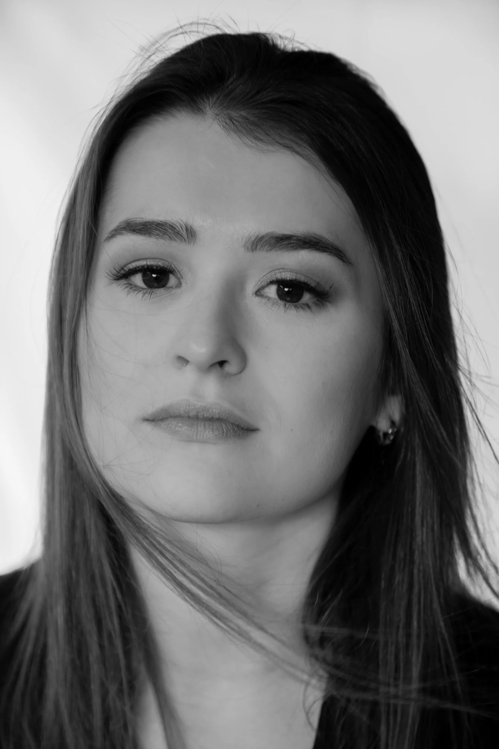 Close-up black and white portrait of a woman with straight hair, wearing earrings, looking at the camera.