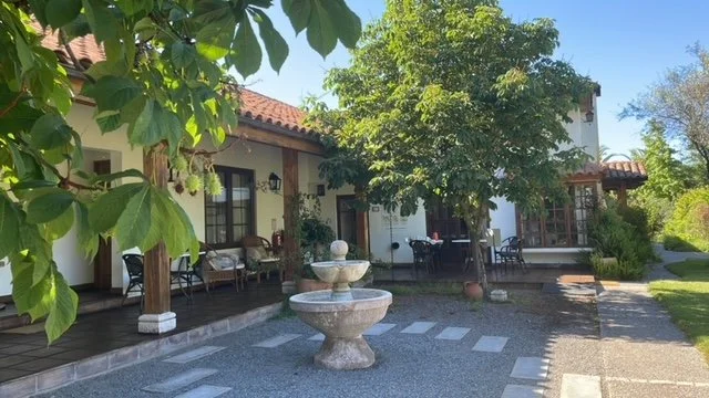 A vineyard house in Chile wine country, with a tiled roof, surrounded by trees and a well-maintained yard with outdoor furniture and a birdbath, visited with Popi Planella and her Chilean Wine Uncovered tours.