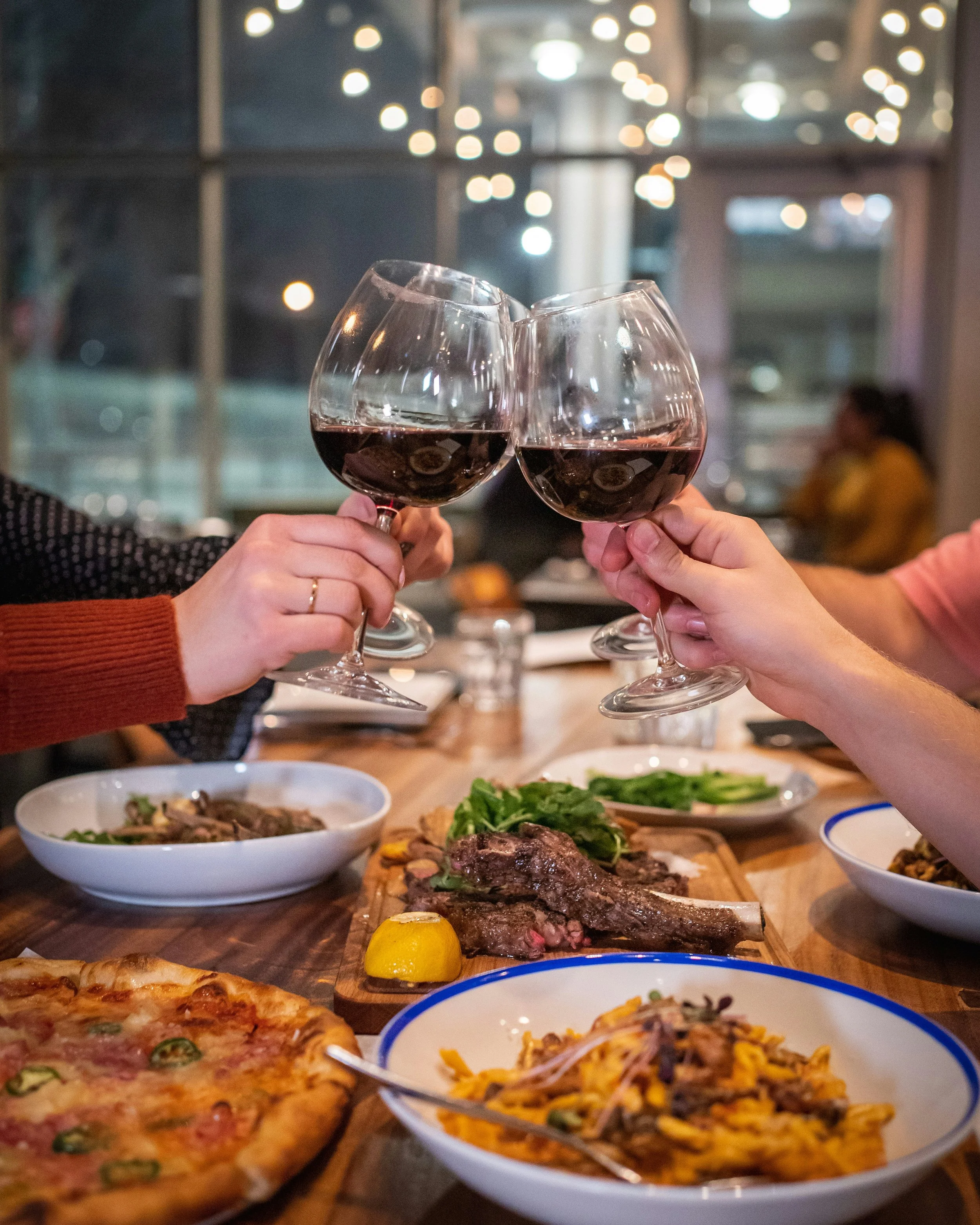 People clinking glasses of red wine in Chile over a meal at a restaurant with Chilean dishes on the table duting a stop with Chilean Wine Uncovered personalized wine tours with Popi Planella.
