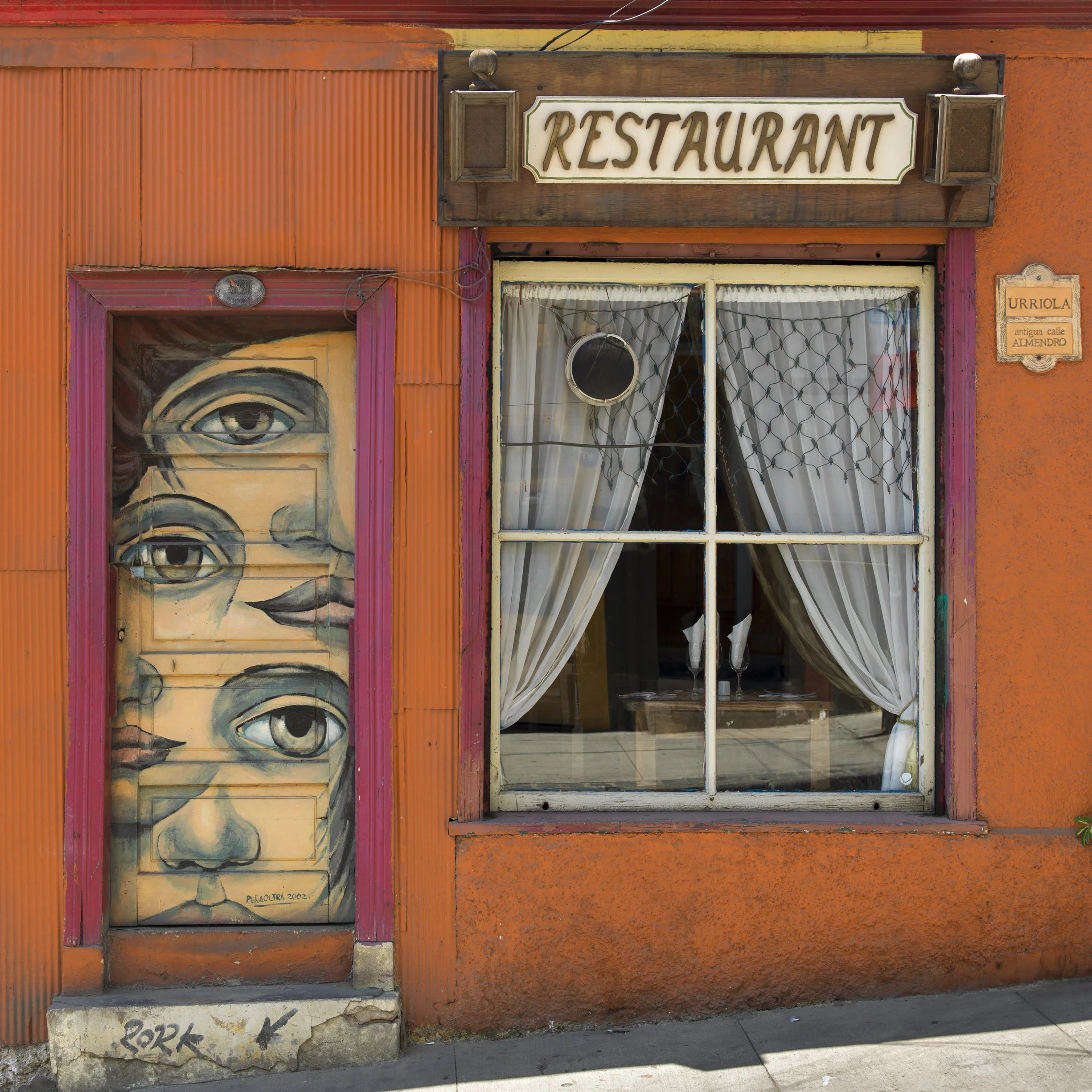 A colorful restuarant building in Chile with an orange exterior, featuring a mural of a face, a stop during a Chilean Wine Uncovered wine country tour with Poppi Planella.