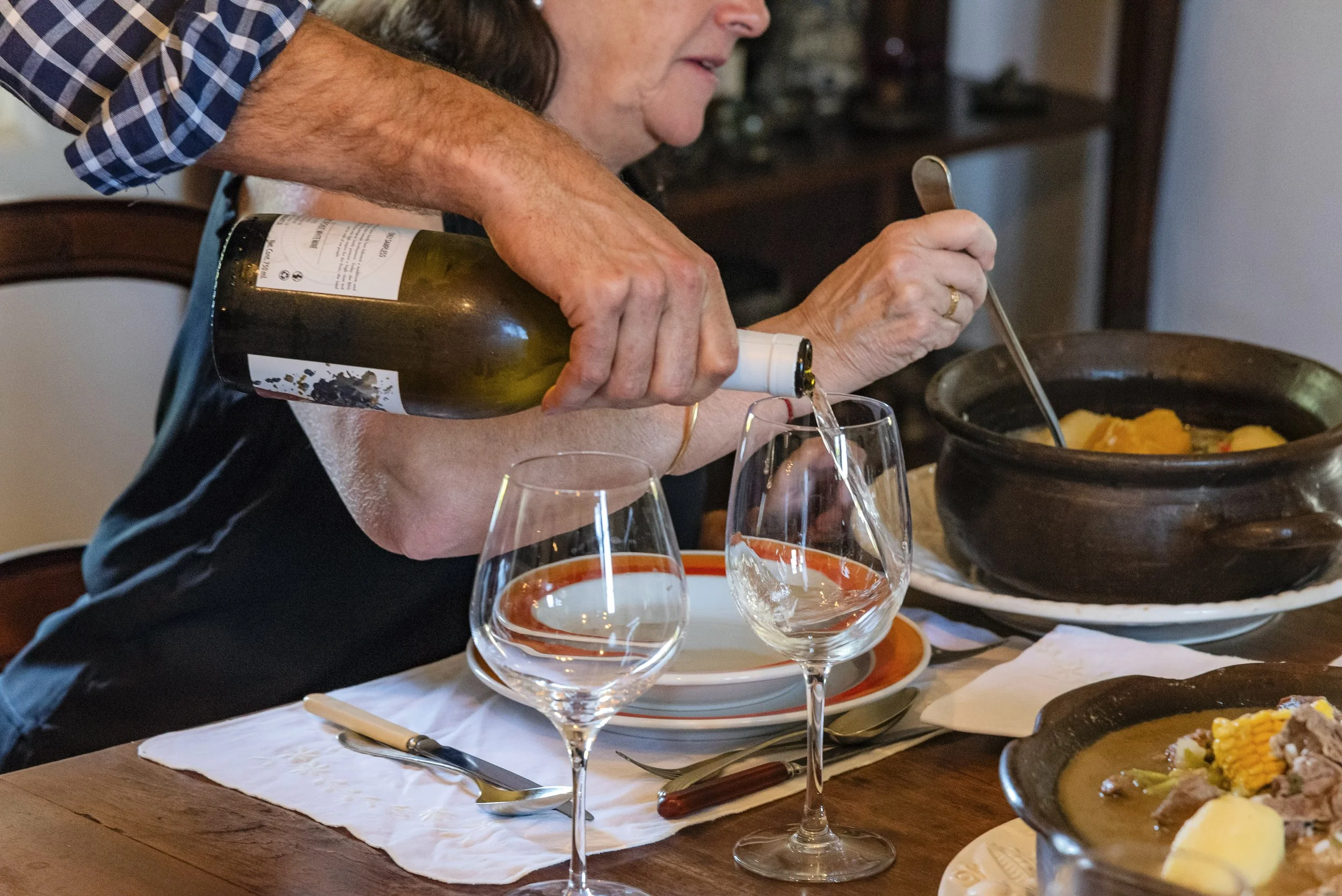 An elderly woman serving wine at a dinner table in a vineyard in Chile, offering local dishes, part of a Chiulean Wine Uncovered wine country tour with Popi Planella.