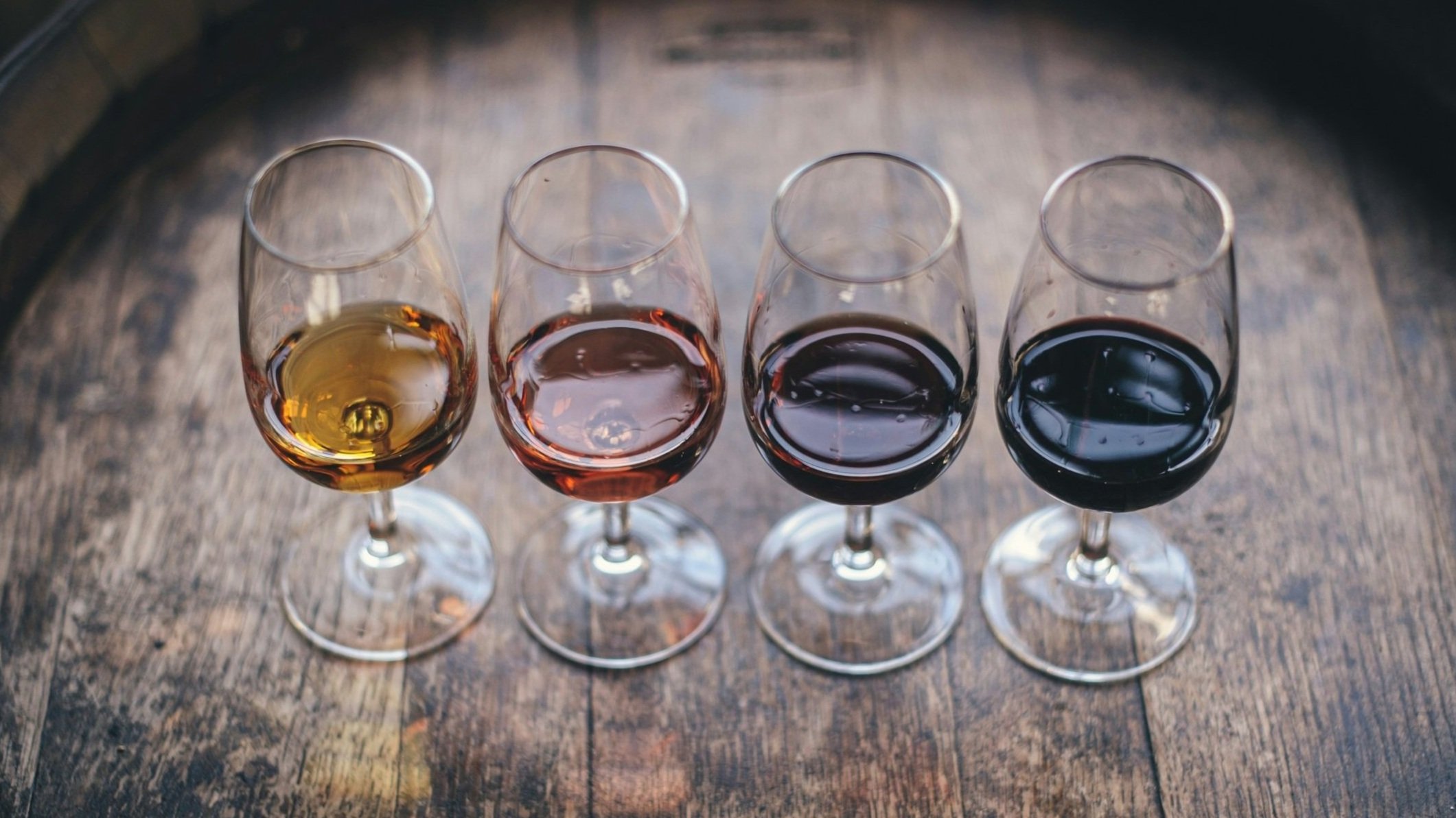 Four glasses of Chilean wine on a rustic wooden table, each with a different color: white, rosé, red, and dark red wine. Taste them all on a tailored wine tour with Popi Planella of Chilean Wine Uncovered.