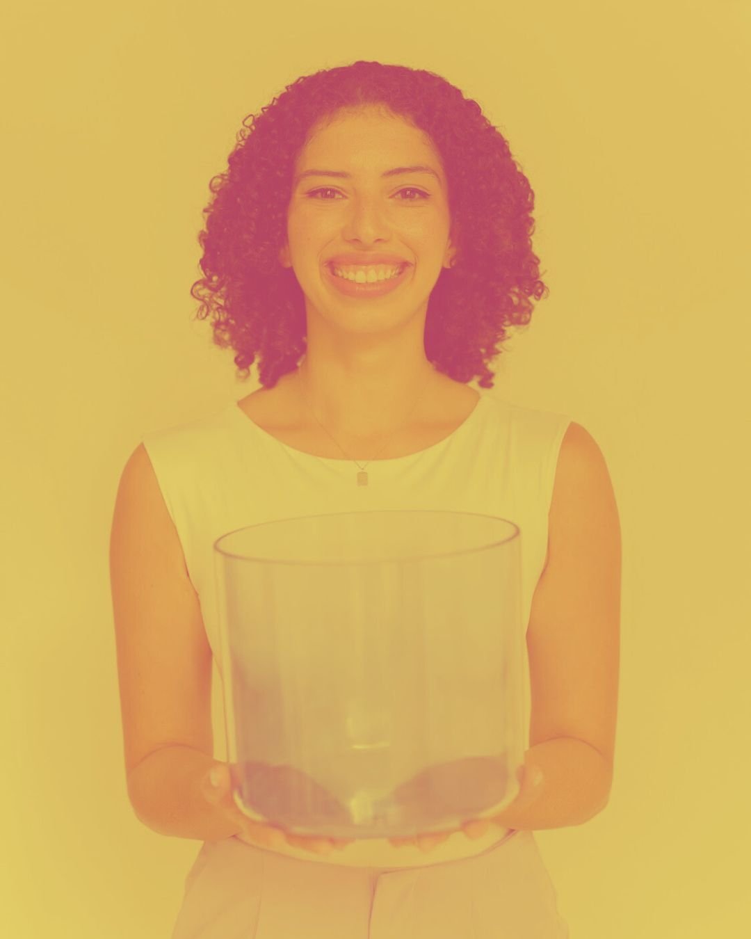 A woman with curly hair smiling and holding a clear glass bowl, standing against a plain background.