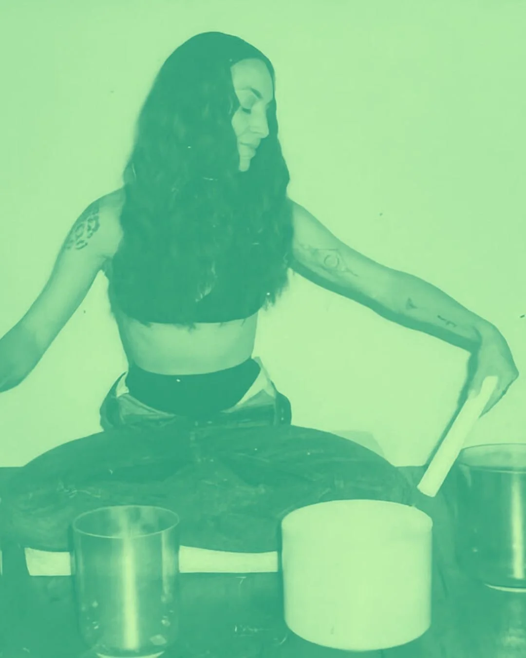 A woman with long dark hair and tattoos on her arms is sitting at a table with candles and drinking a beverage through a paper tube.