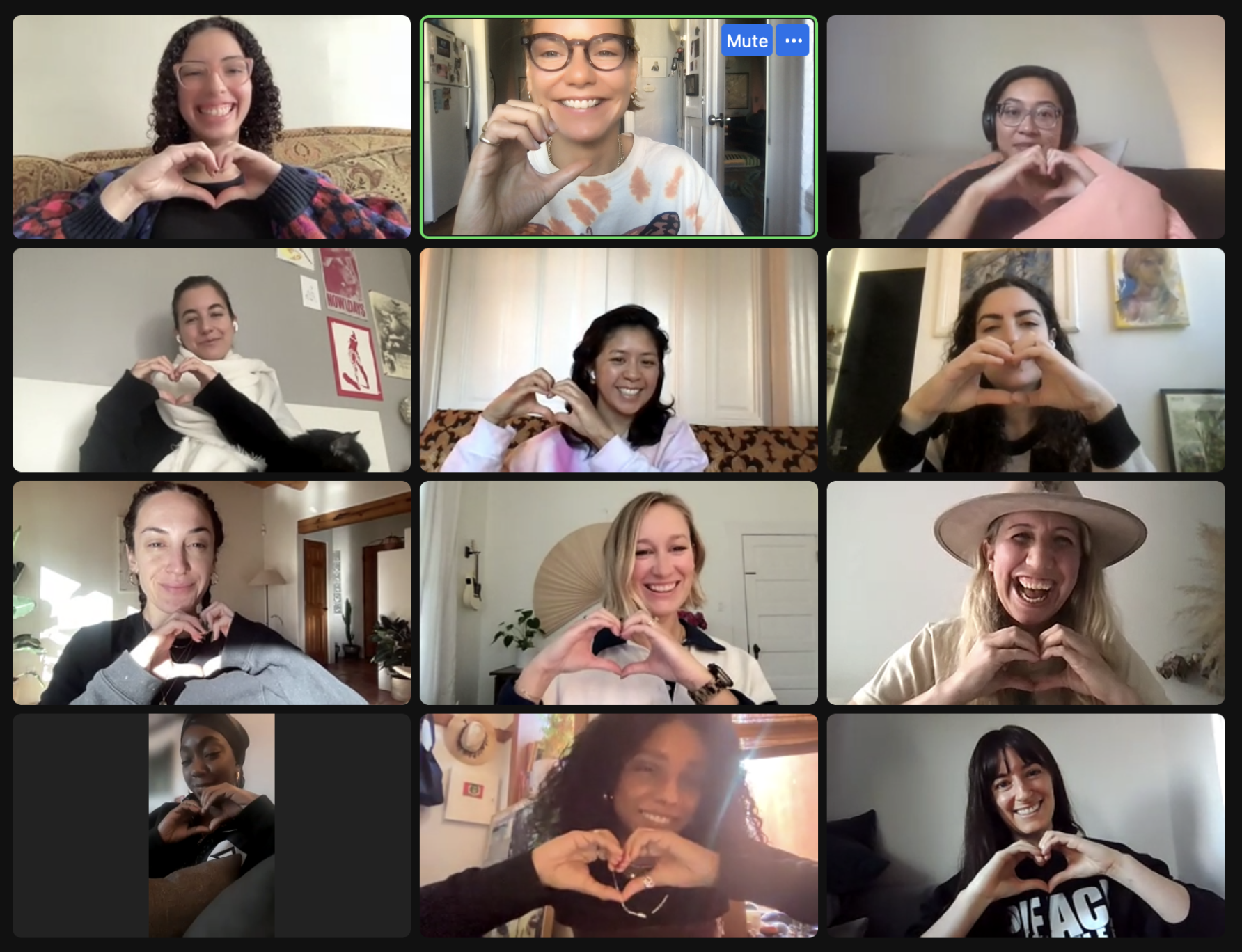 Screenshot of a virtual meeting with 13 women, all making heart shapes with their hands, smiling, and appearing happy.
