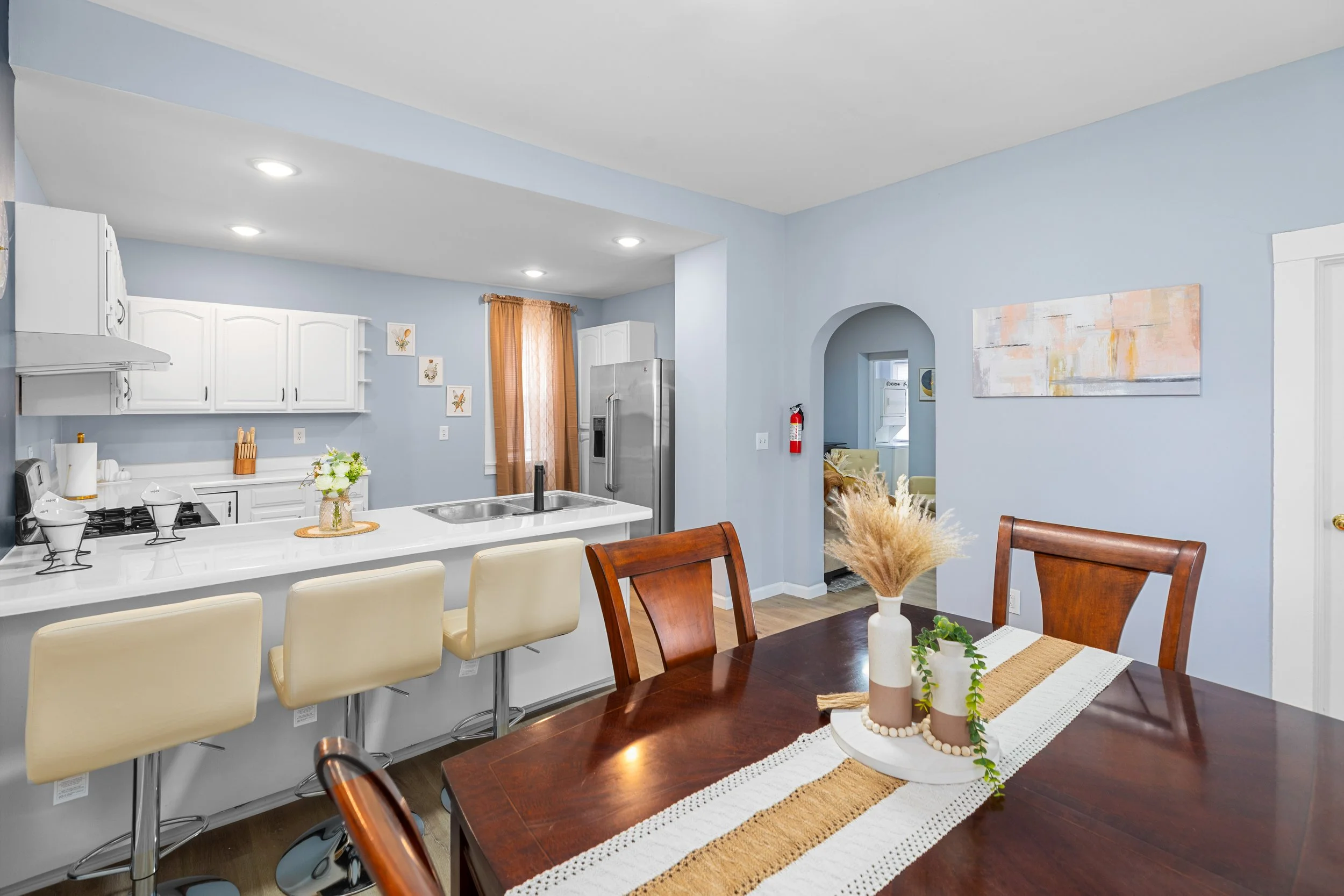 Kitchen and dining area with light blue walls, white cabinets, a stainless steel refrigerator, and a dark wooden dining table with chairs.