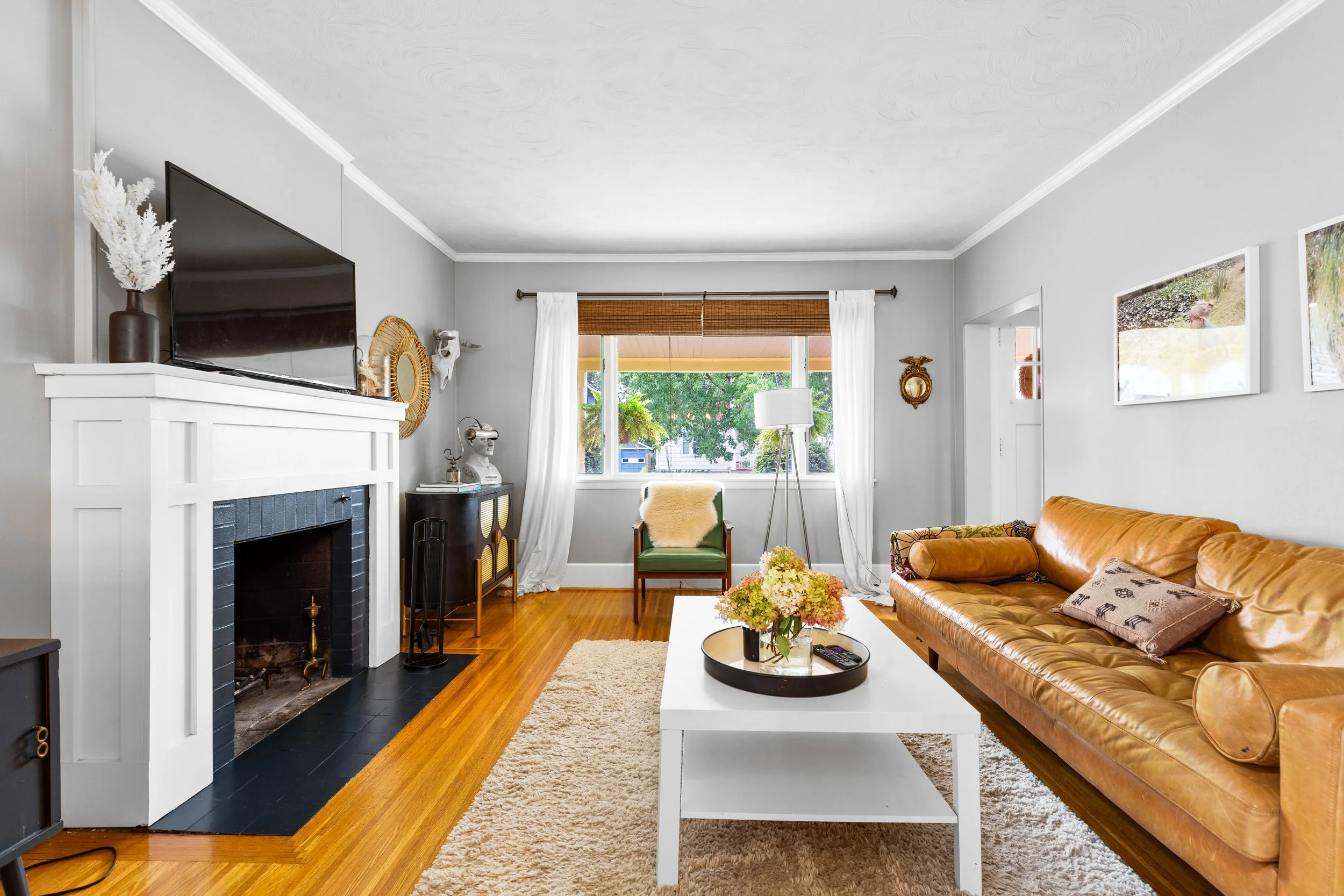 Living room with a leather sofa, white coffee table with a flower arrangement, fireplace, armchair near window, and wall art