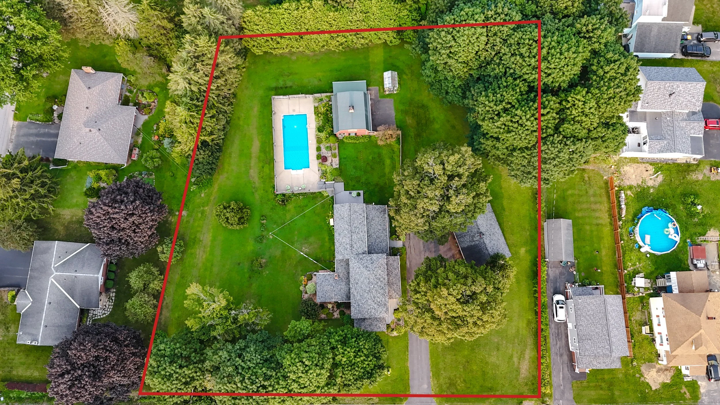Aerial view of a suburban backyard outlined in red, featuring a swimming pool, a house, a trampoline, and surrounding trees and neighboring houses.