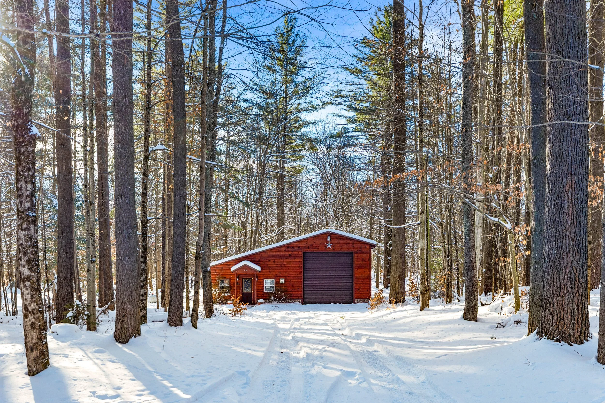A rustic cabin set in the foothills of the Adirondacks while snow surrounds it with trees and blue skies